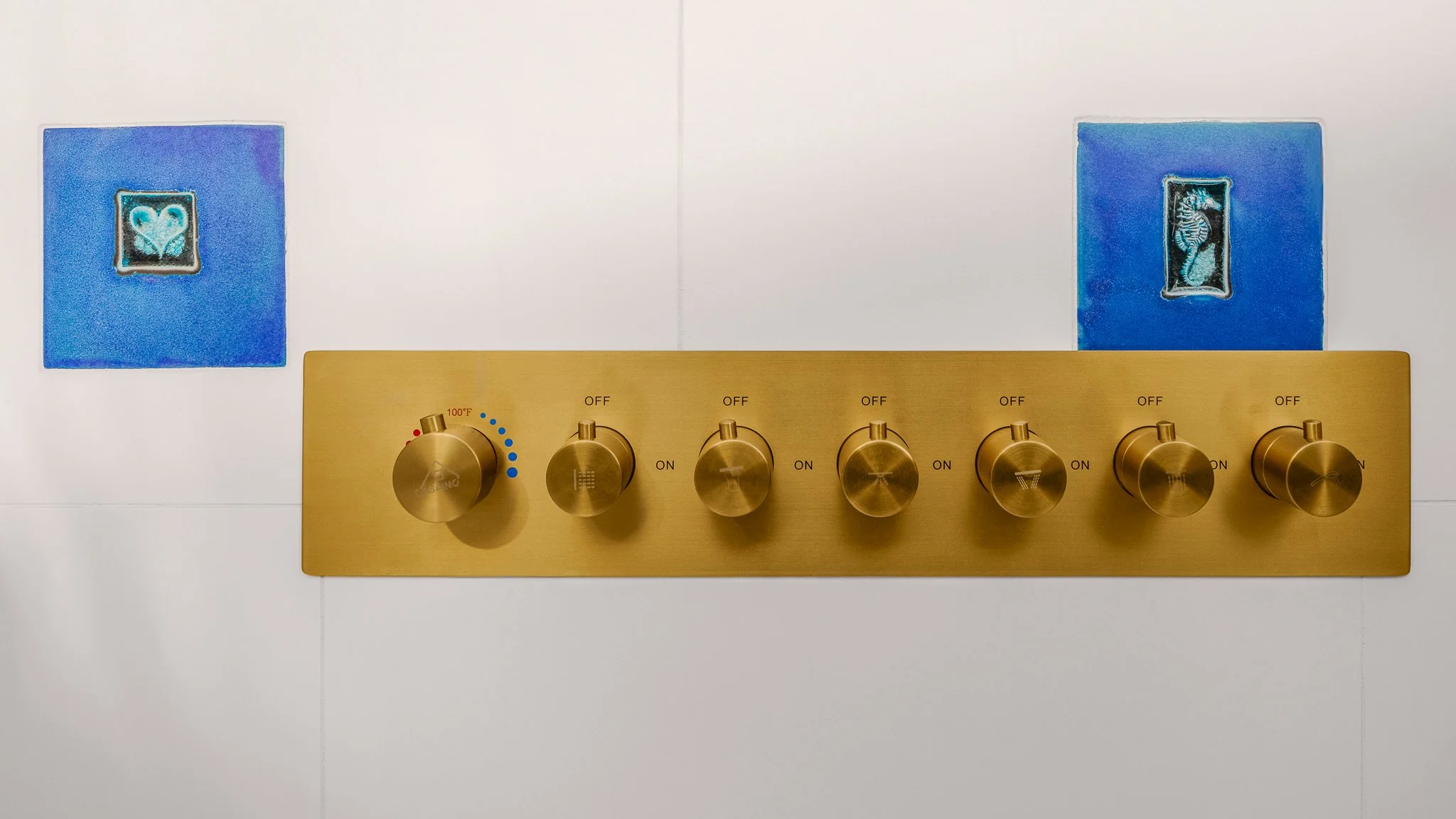 Brushed brass shower controls set between two handmade blue tiles.