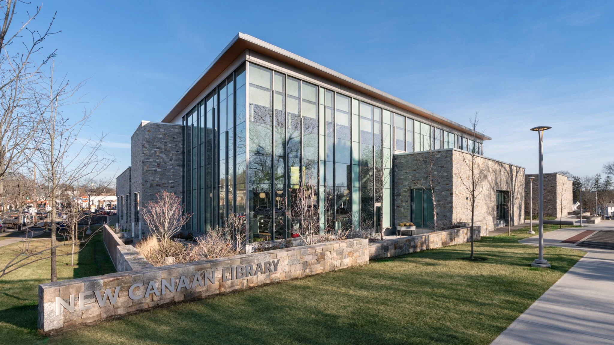 Glass facade behind the front lawn and stone sign wall.