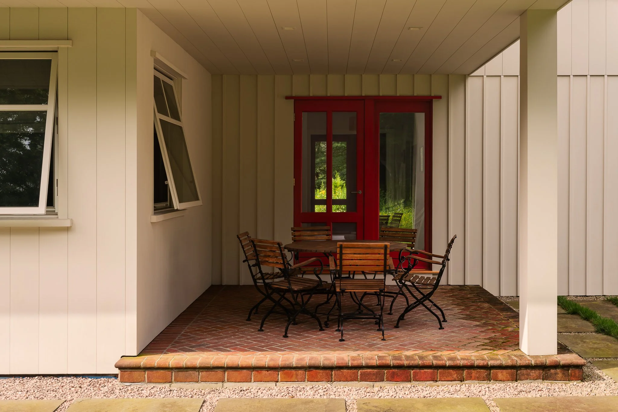 Covered brick patio with an outdoor dining table and red French doors.
