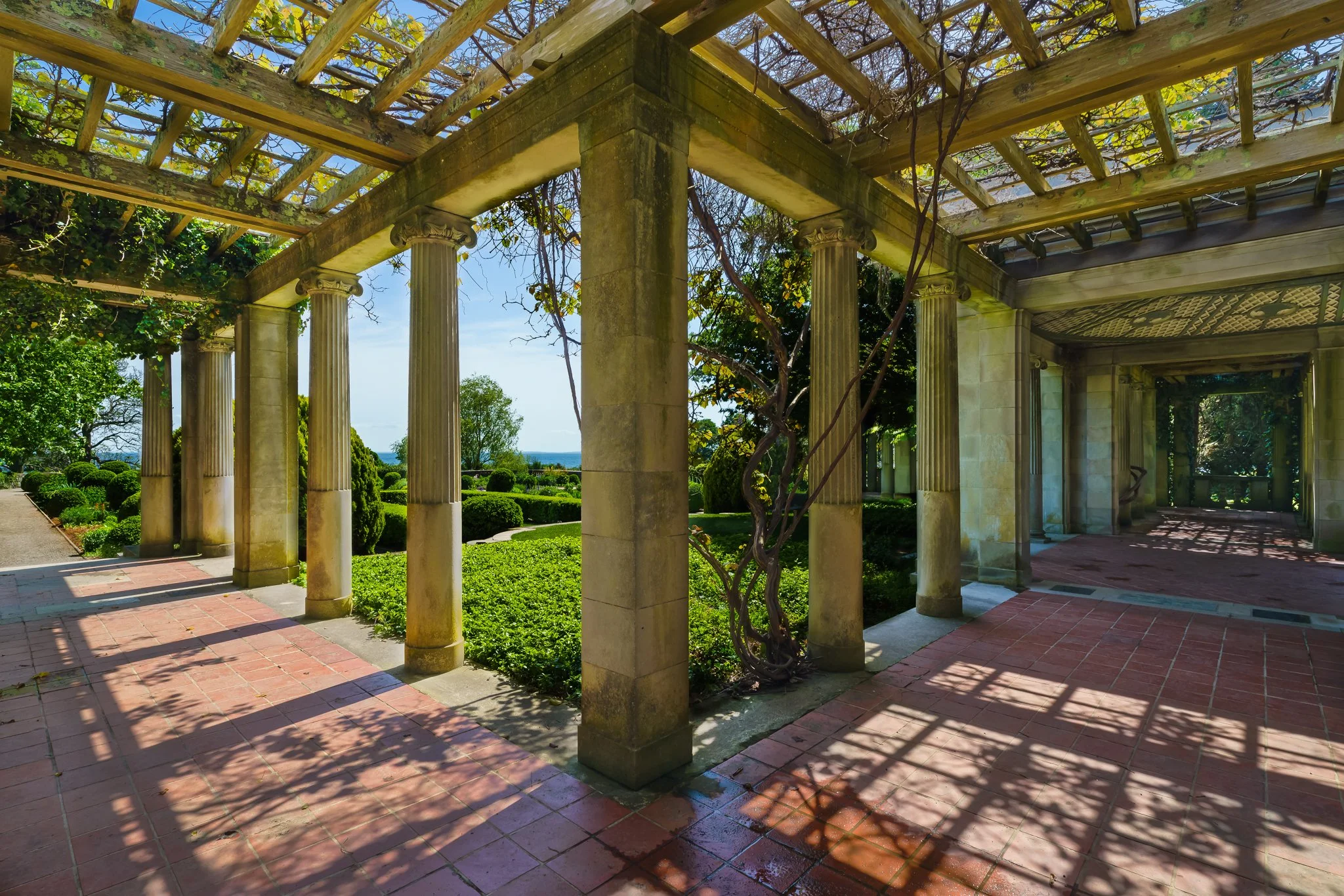 Pergola walkway at Harkness Memorial State Park with stone columns and dappled sunlight across a brick floor.