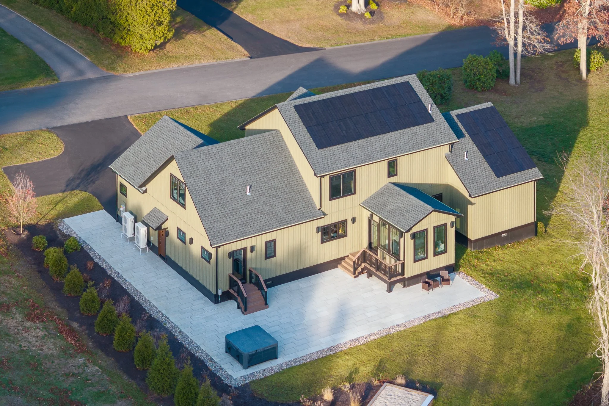 Aerial drone view of the back of the house with solar panels, a stone patio and a hot tub.