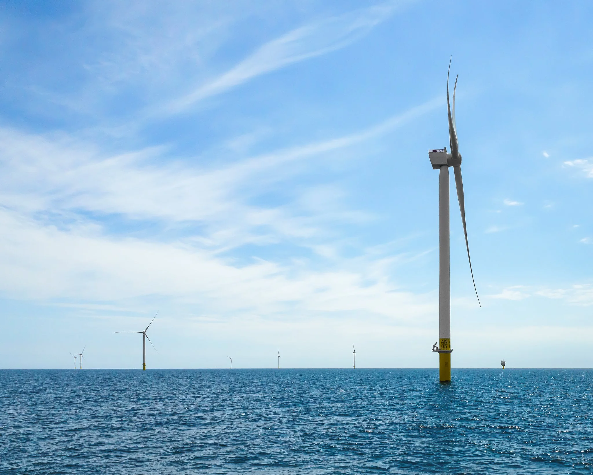 Low view across the water of a nearby turbine with the rest of the wind farm on the horizon.