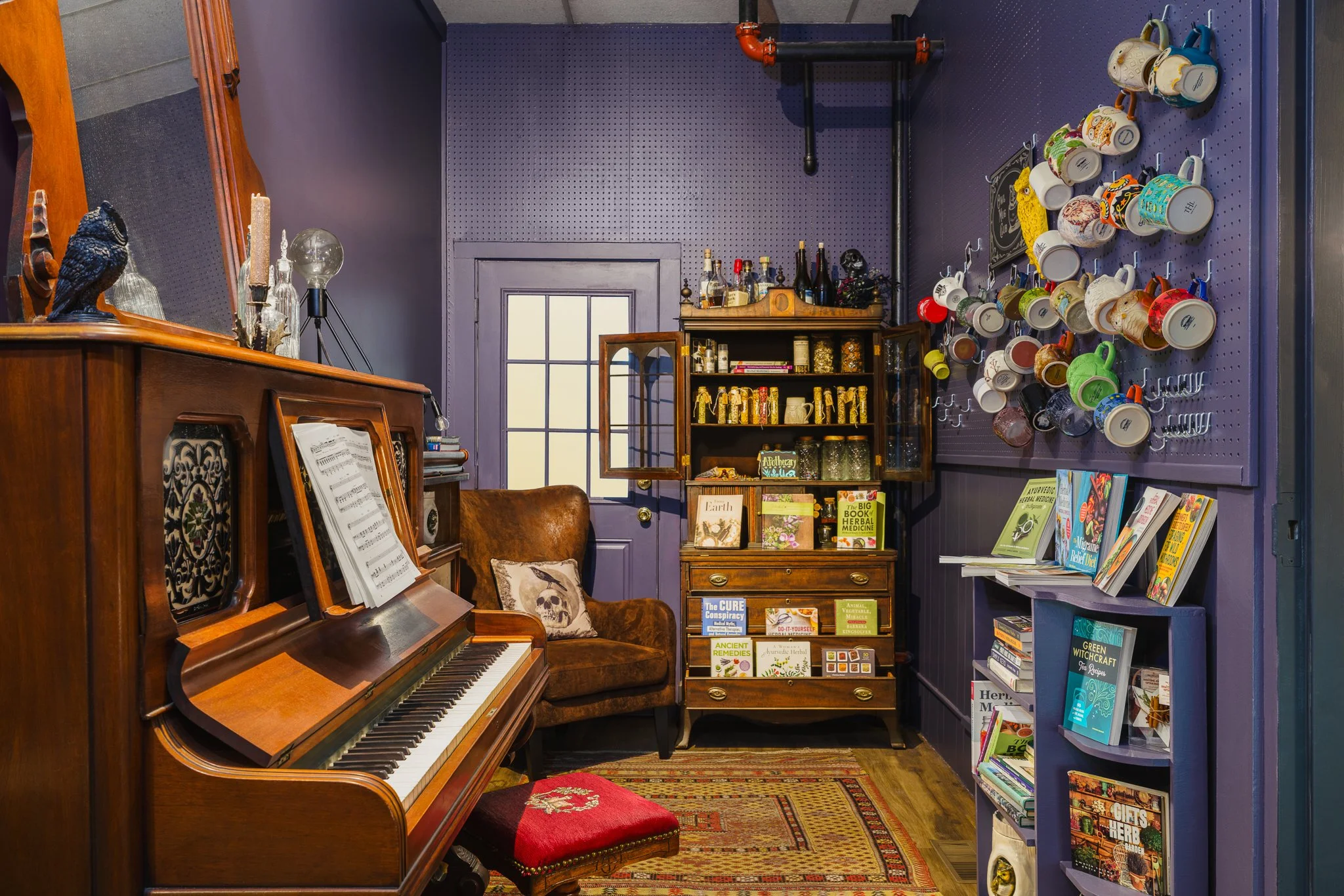 Upright piano beside shelves of coffee mugs and books.