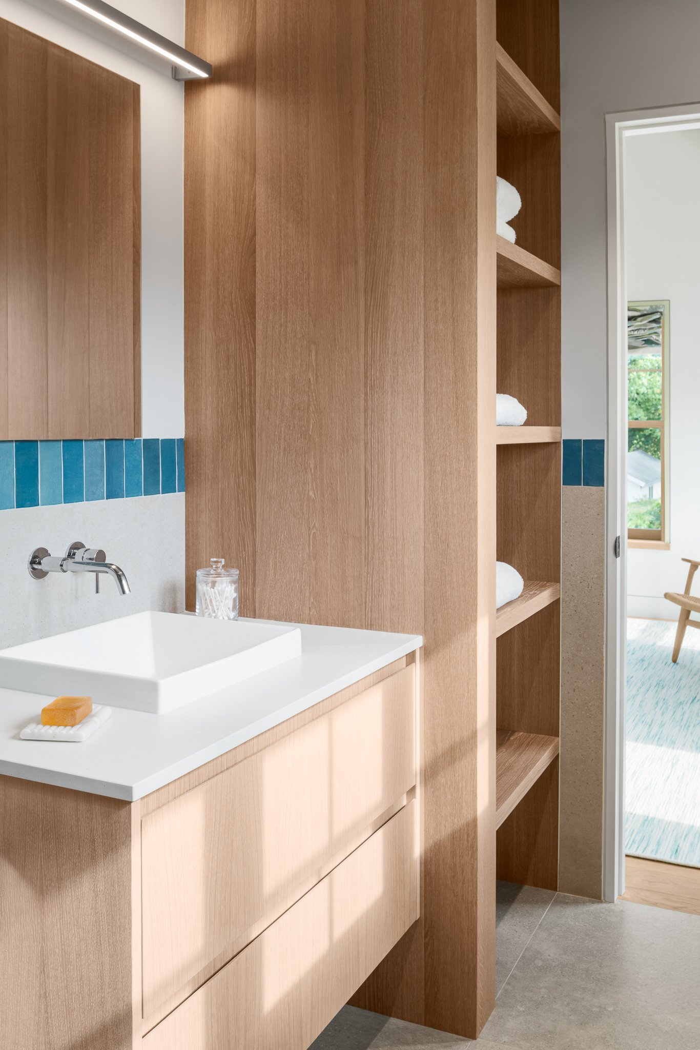 Wood vanity with open towel storage and a strip of blue tile behind the sink.