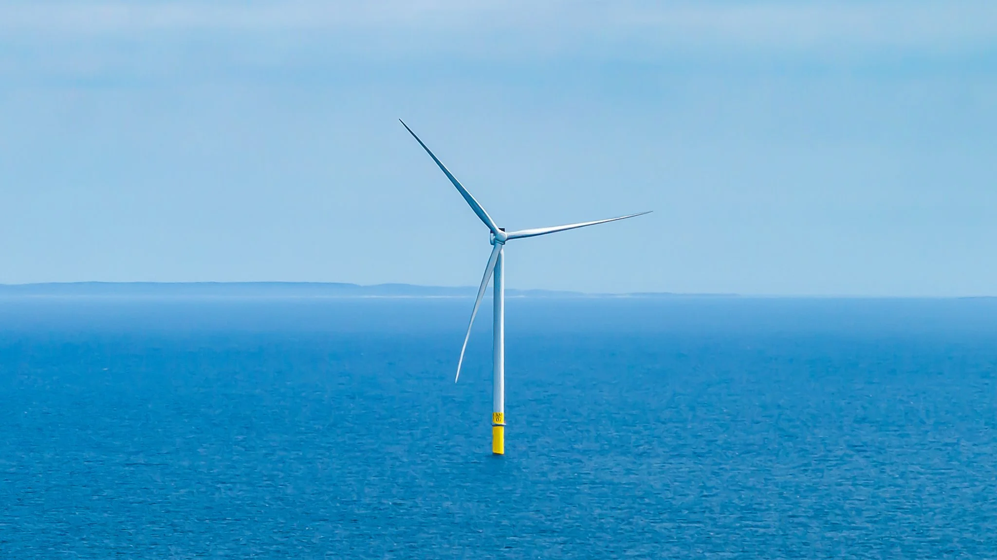 Wind turbine in calm blue water with a faint shoreline on the horizon.