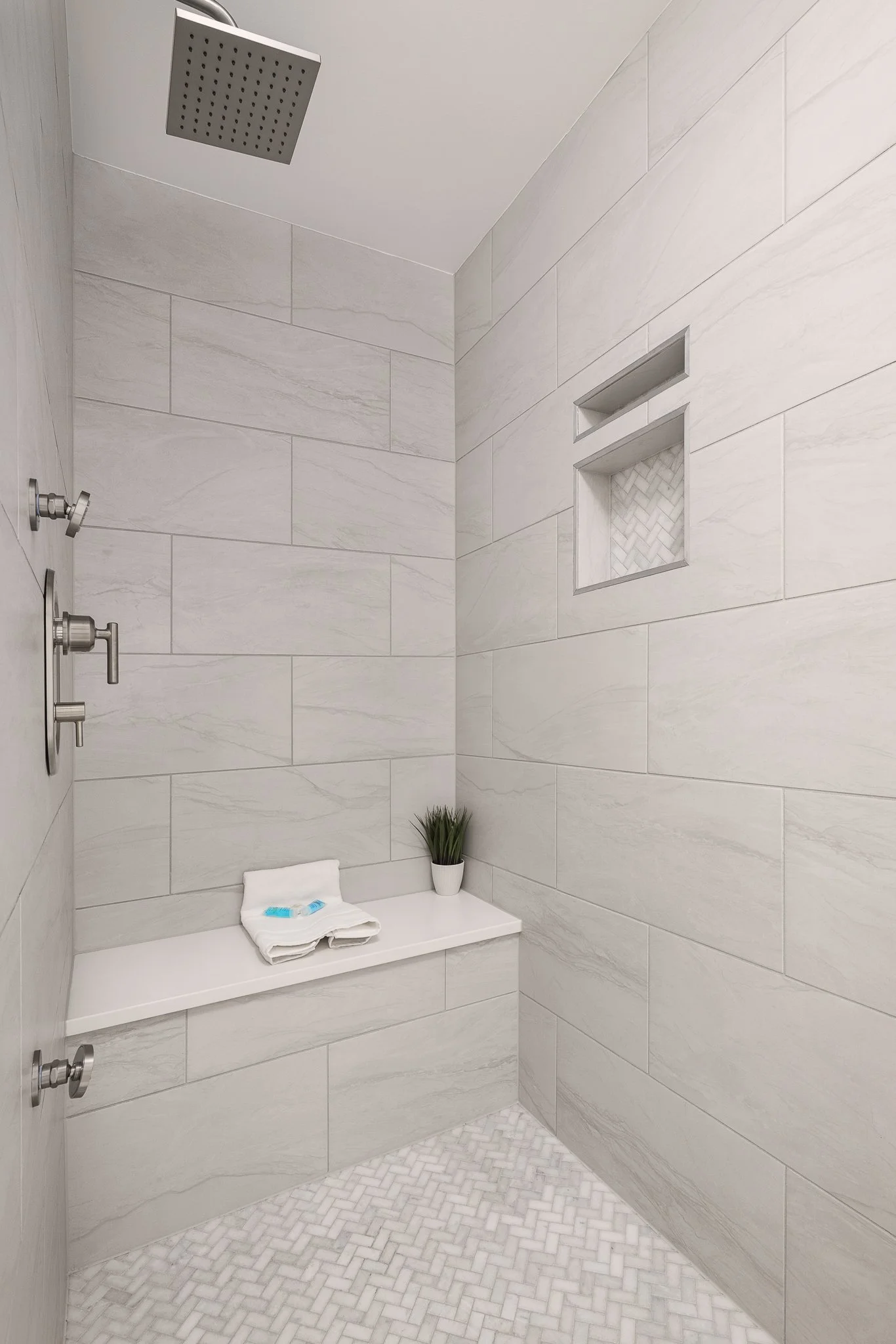 Walk-in shower with large gray tile, a built-in bench and a rain showerhead.