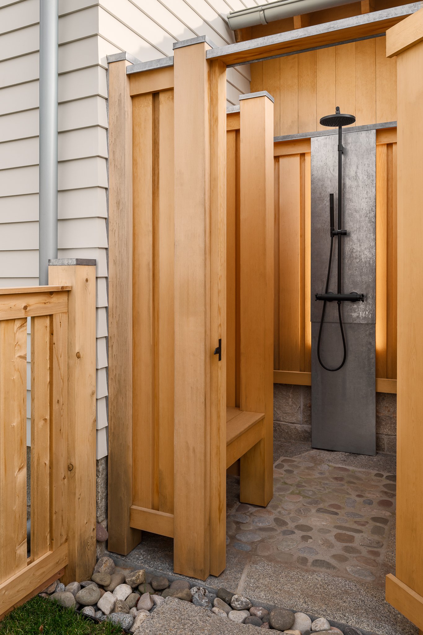 Wood-walled outdoor shower with a stone floor and backlit panel.