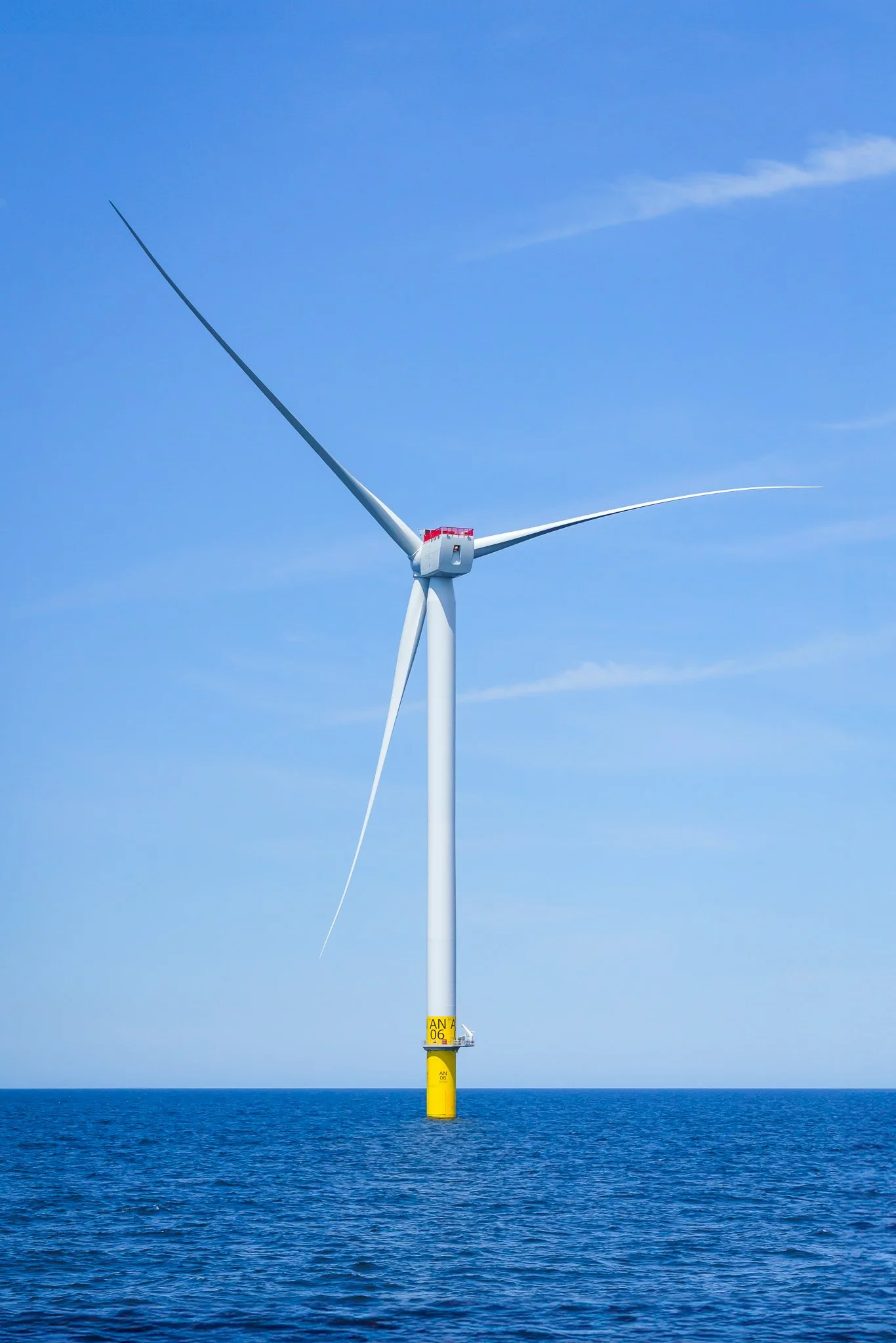 Full height of a wind turbine, from yellow foundation to blade tip, against clear blue sky.