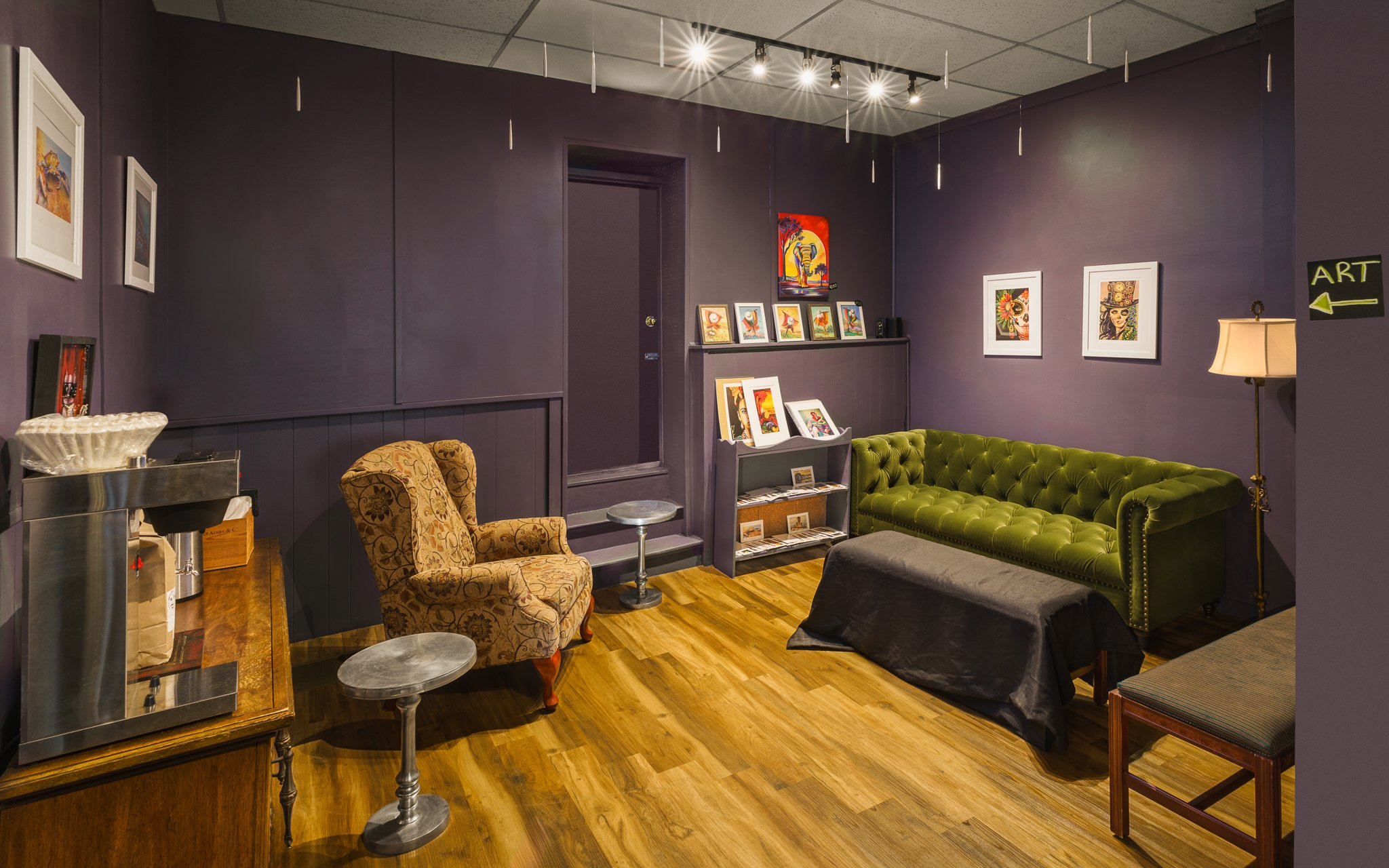 Reading room at The Golden Owl with a green velvet sofa and armchairs against dark purple walls.