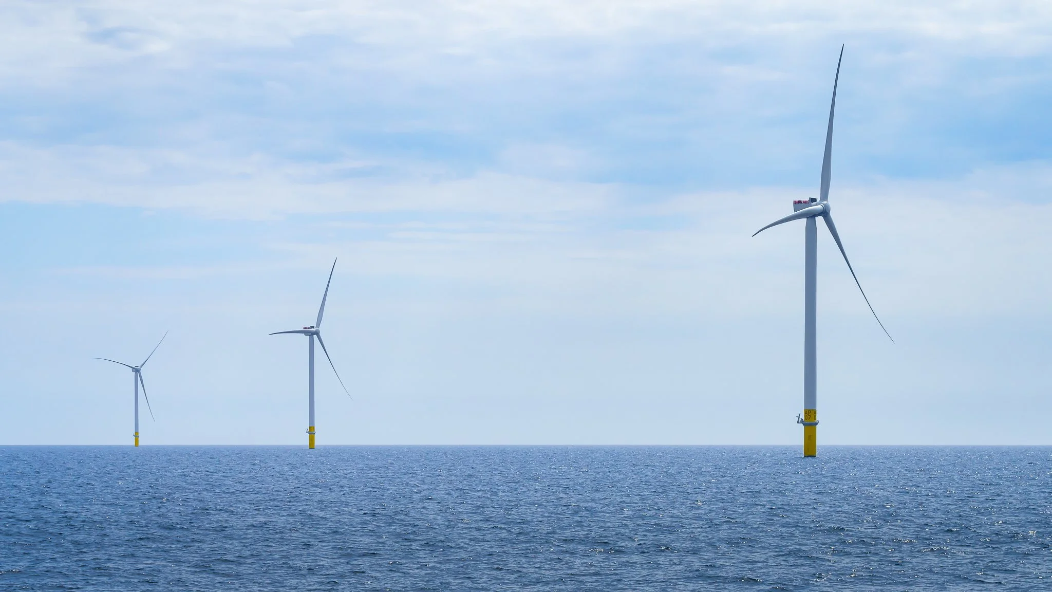 Three wind turbines in a line, receding across the water.