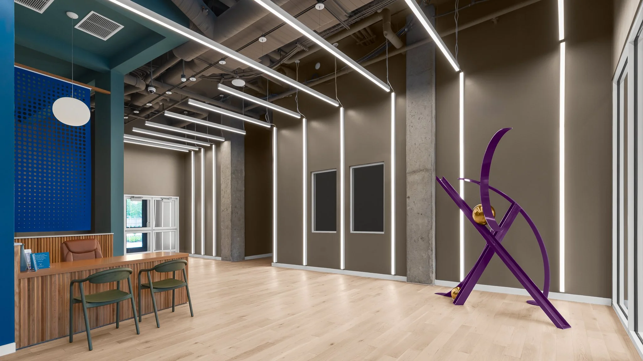 Lobby with a purple sculpture, vertical light tubes on green walls and a concierge desk.