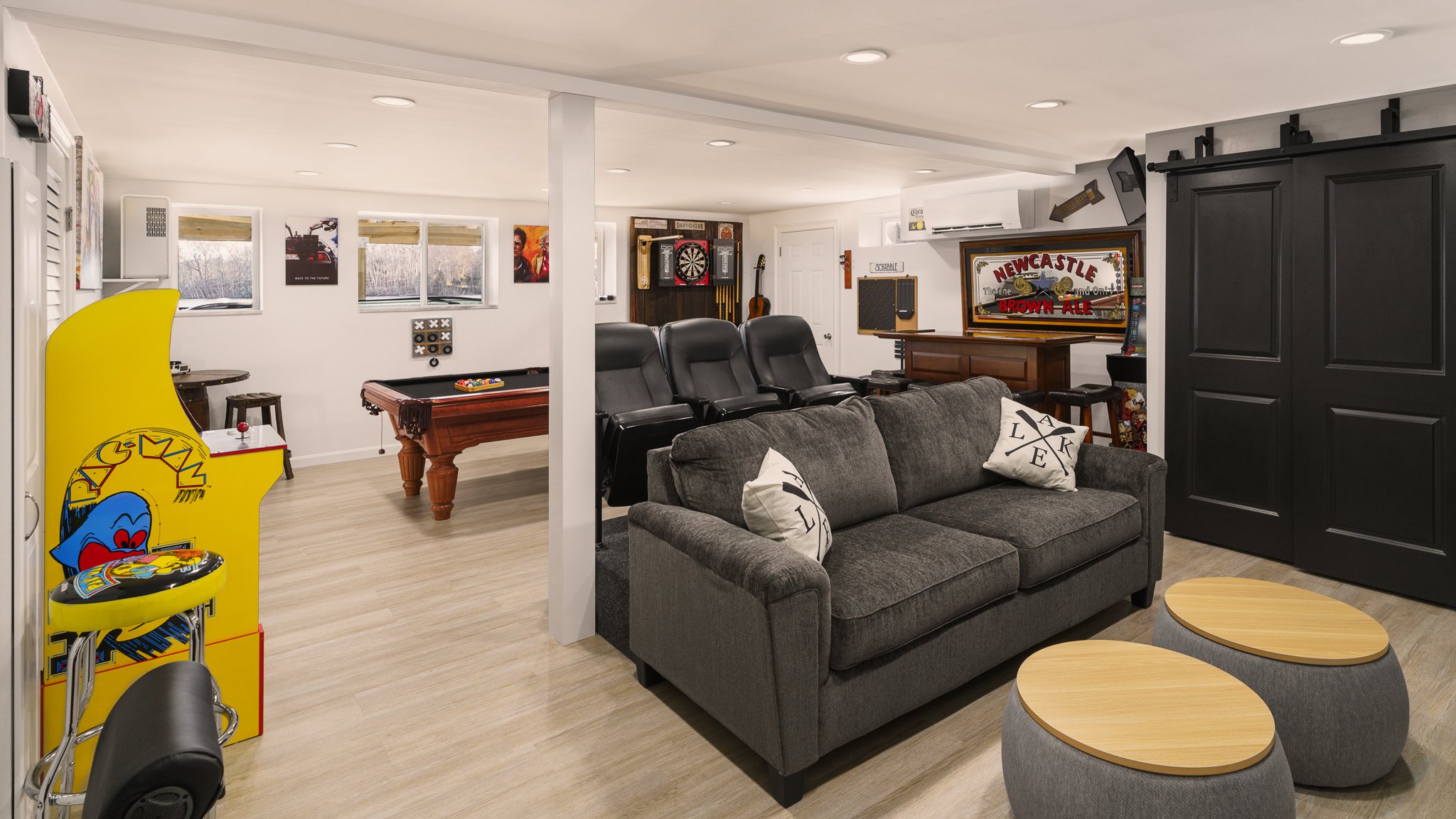 Basement game room with a sectional couch, arcade machine and theater chairs.