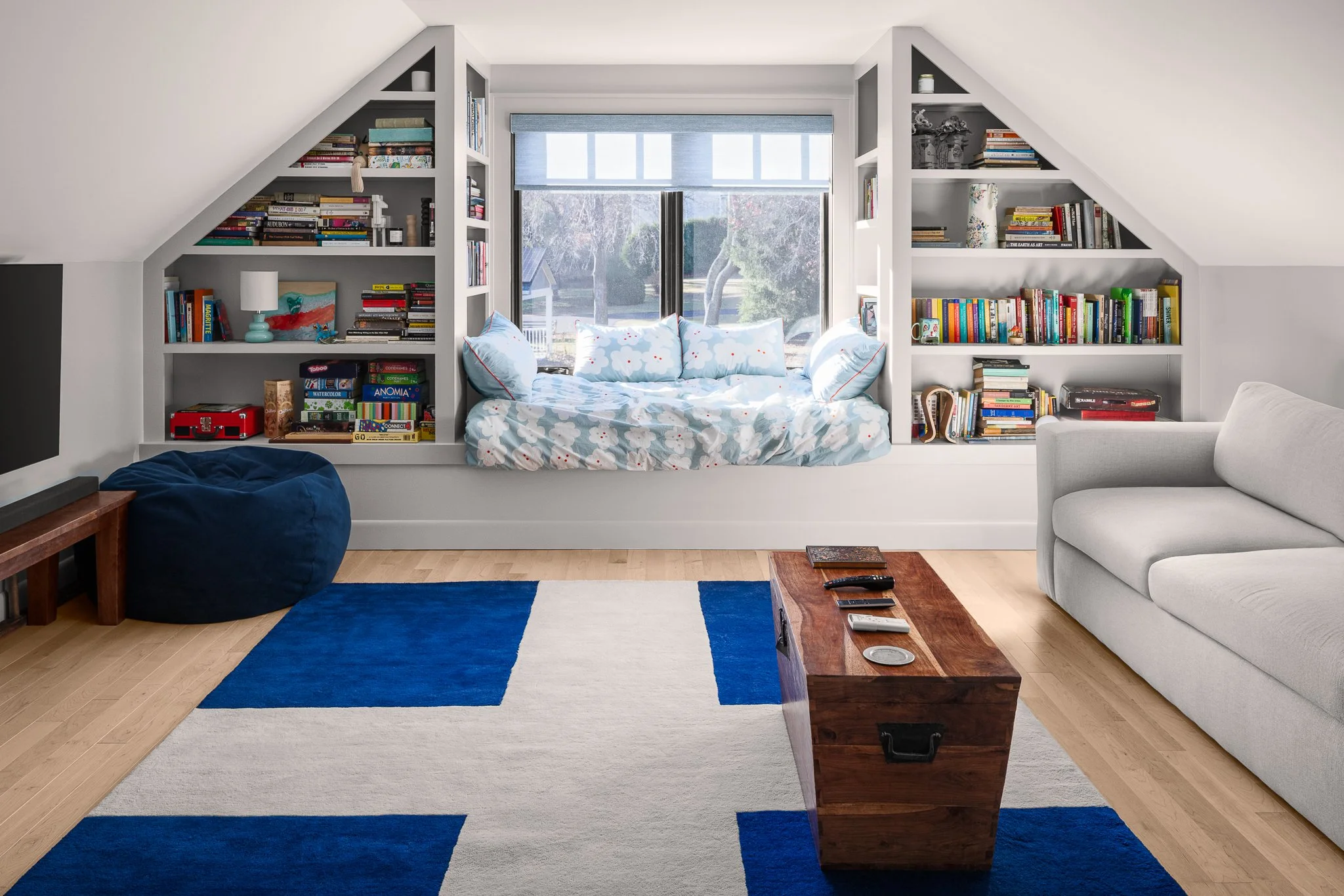 Attic playroom with a window day bed between built-in bookshelves and a blue and white rug.