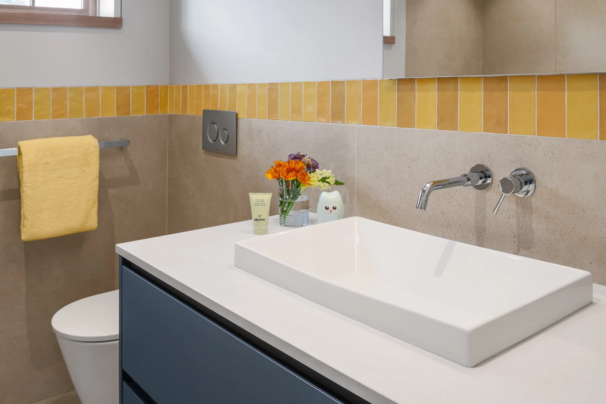 Vessel sink on a blue vanity with a band of yellow tile.