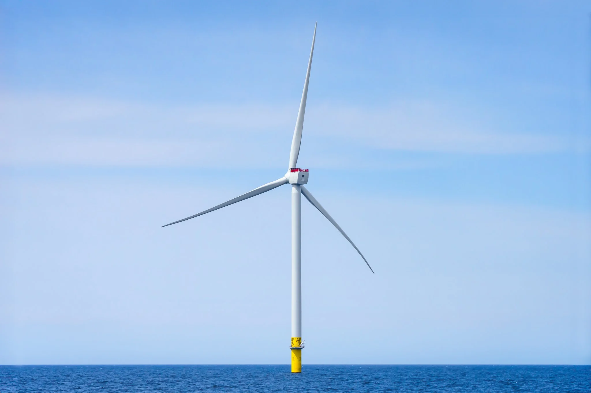 Single wind turbine on a yellow foundation against a pale blue sky.