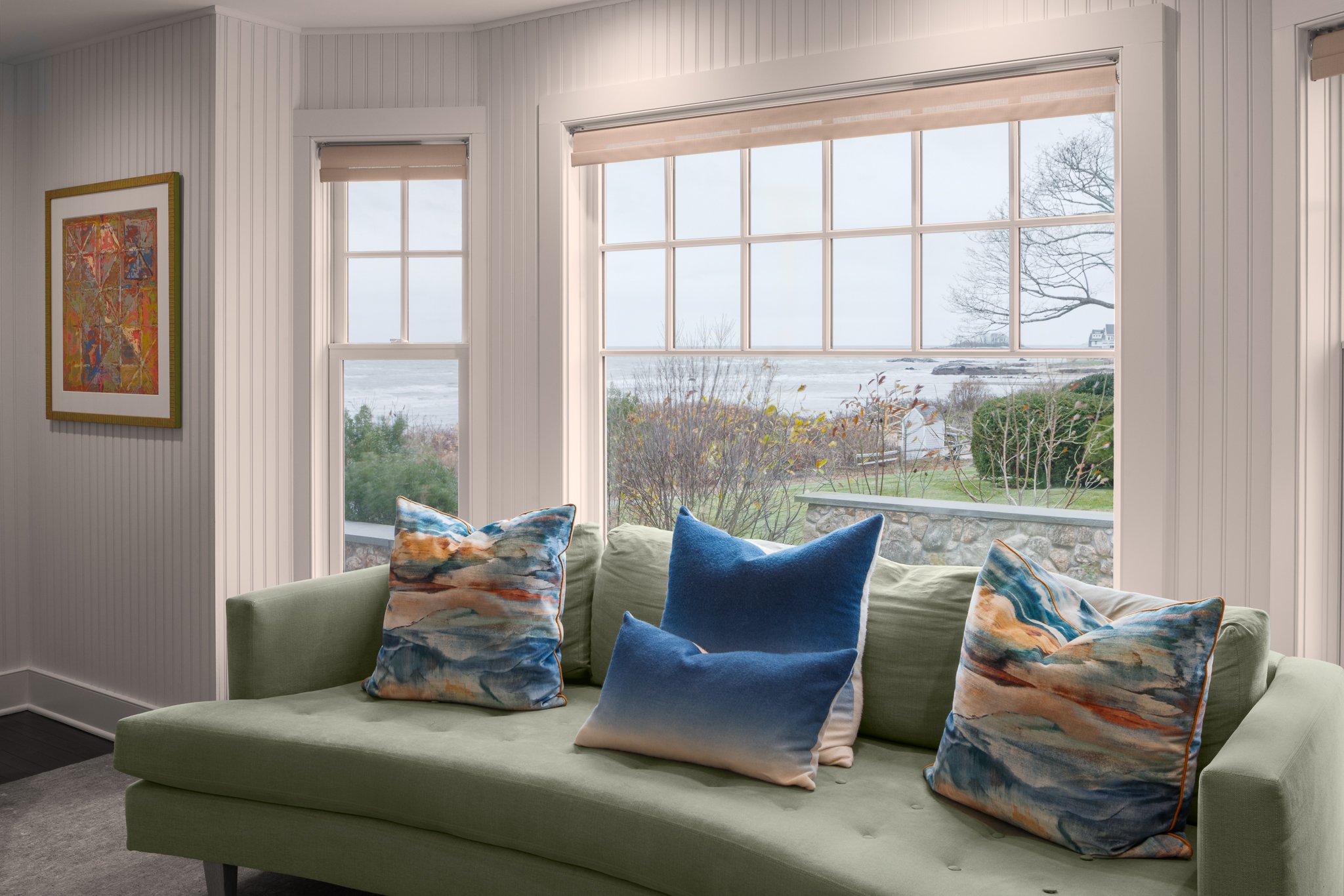 Green sofa beneath a wide window looking out to the shoreline.