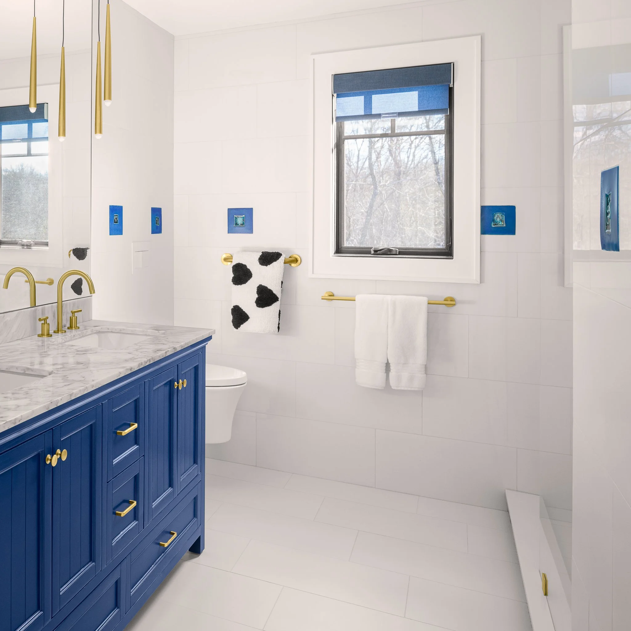 Bathroom with a navy vanity, brass pendants and scattered blue tiles.