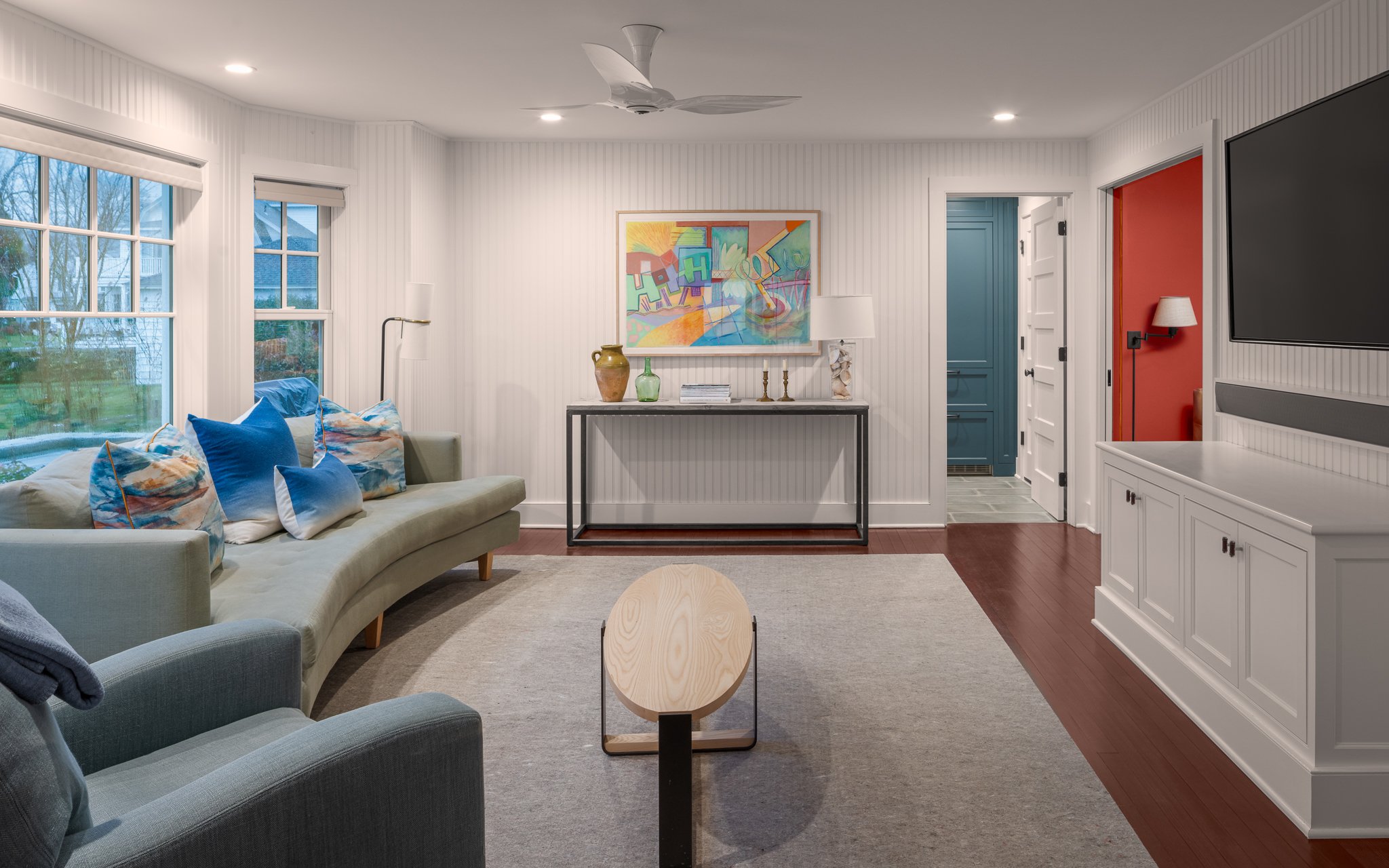 Family room with a sofa and TV, looking toward a red-walled office nook.