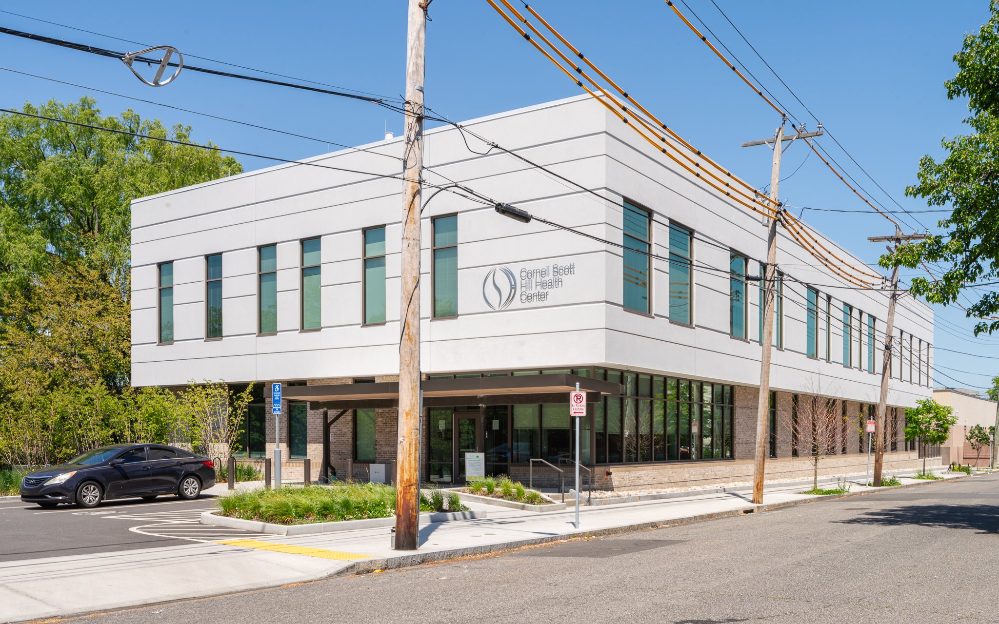 Before: raw capture of the Cornell Scott-Hill Health Center with a utility pole, wires and a parked car in view.