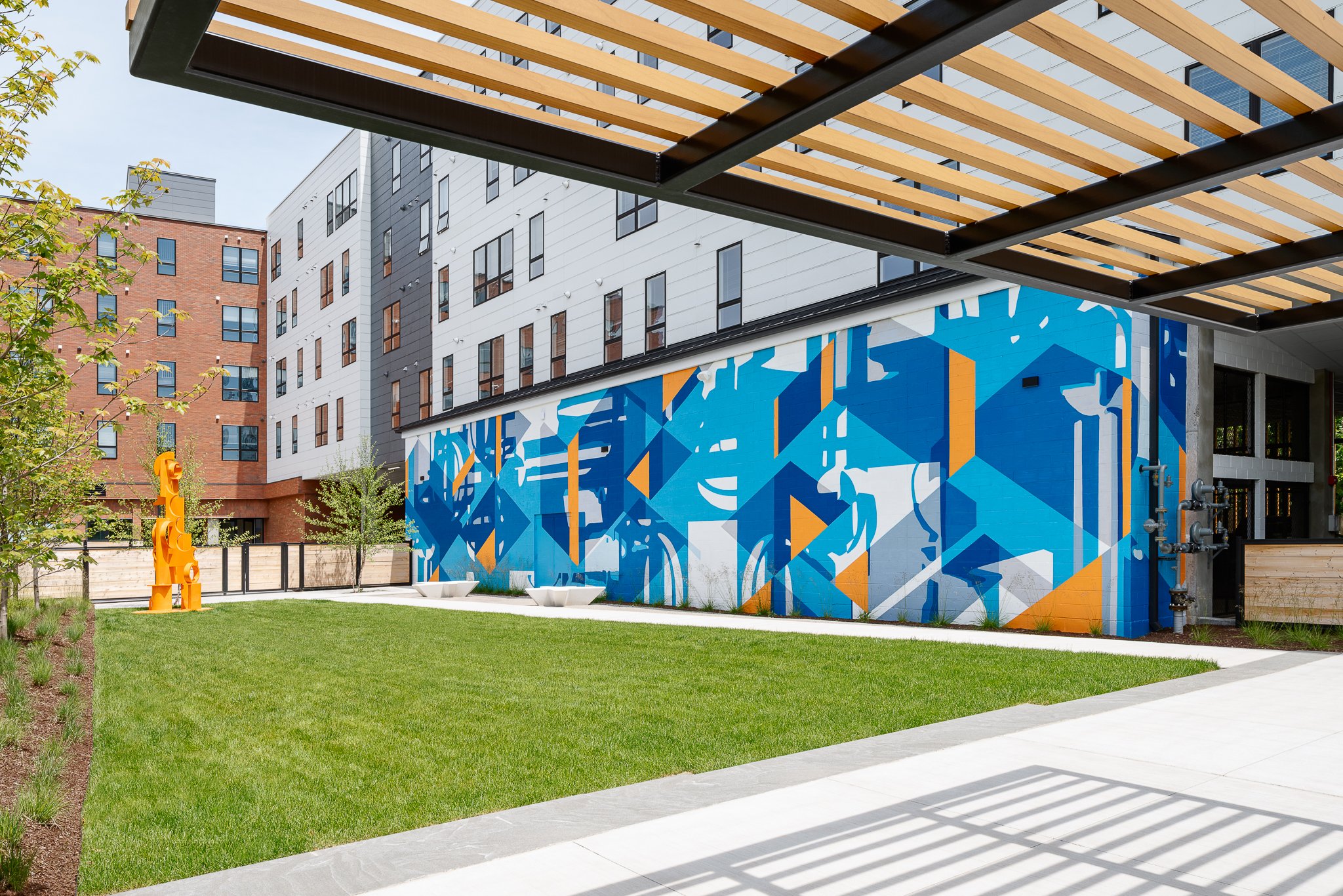 Cadence on Canal courtyard with a bold blue mural, an orange sculpture and a slatted pergola.