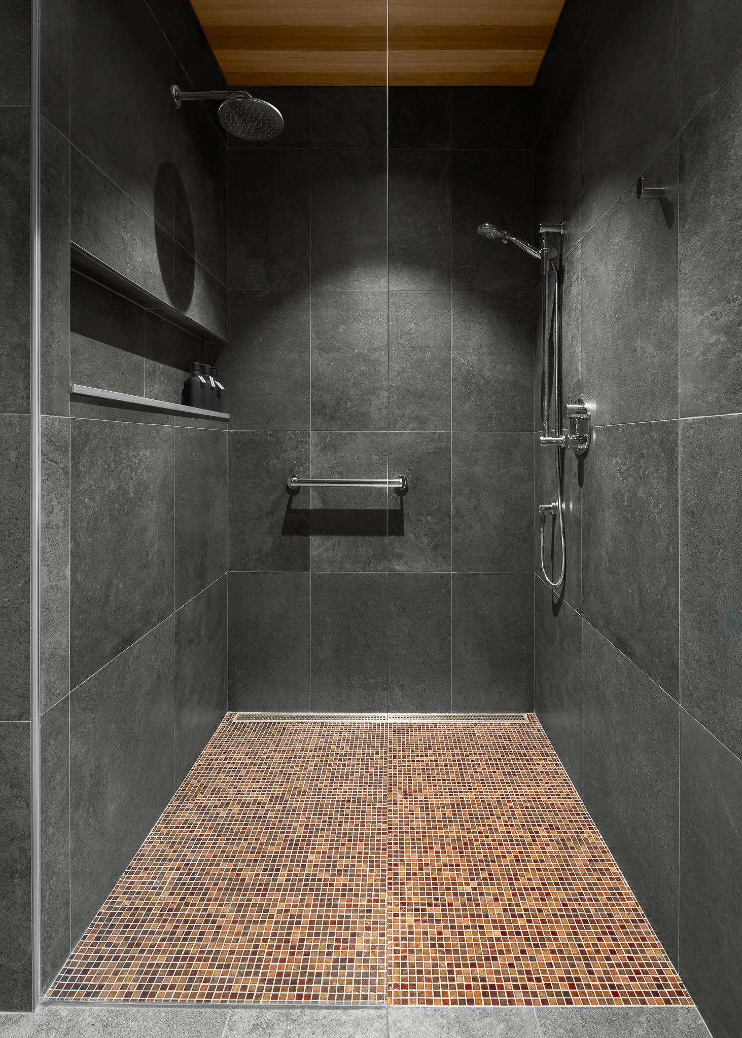 Dark stone shower with a wood ceiling and a warm-toned mosaic floor.