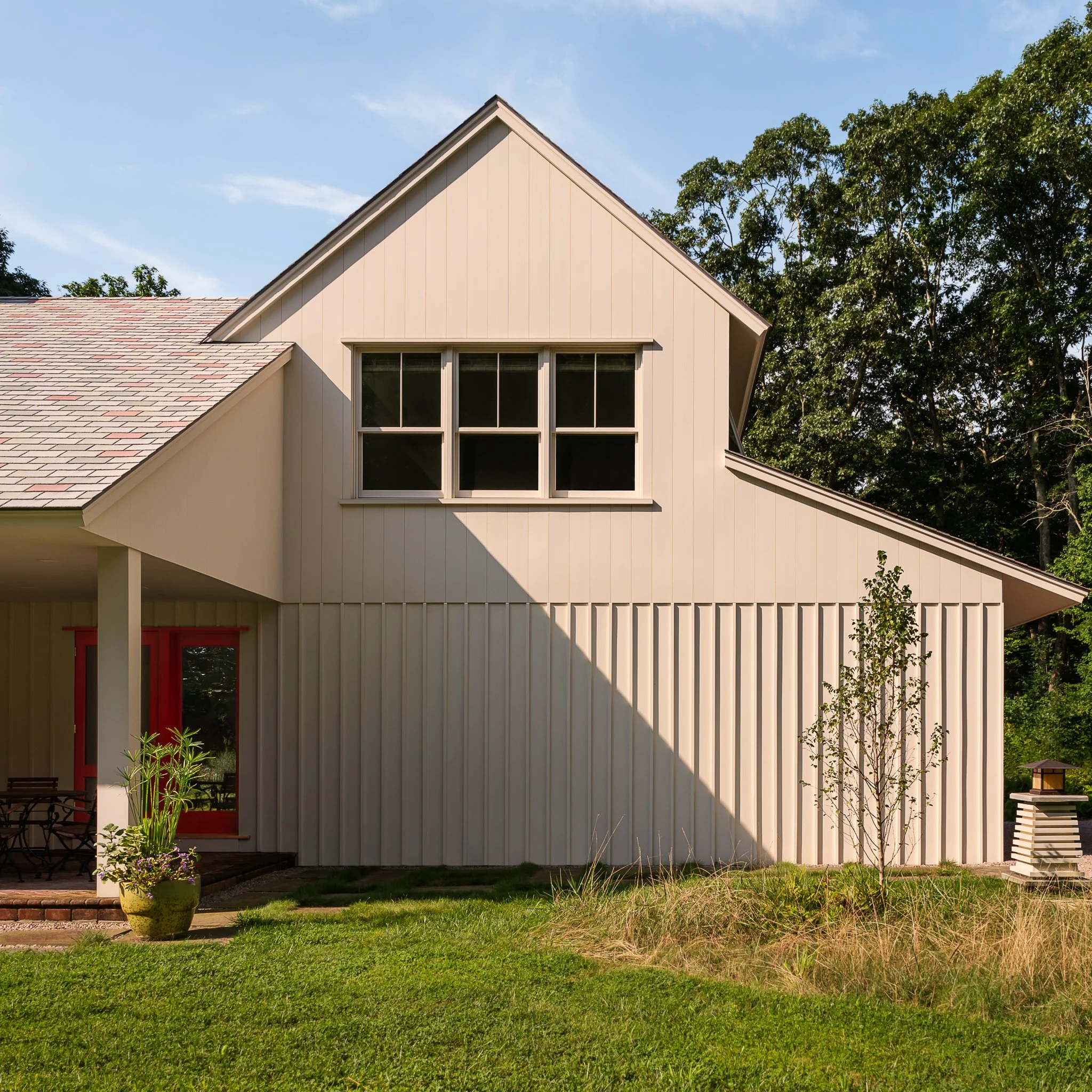 Gabled exterior with board and batten siding and a red door.