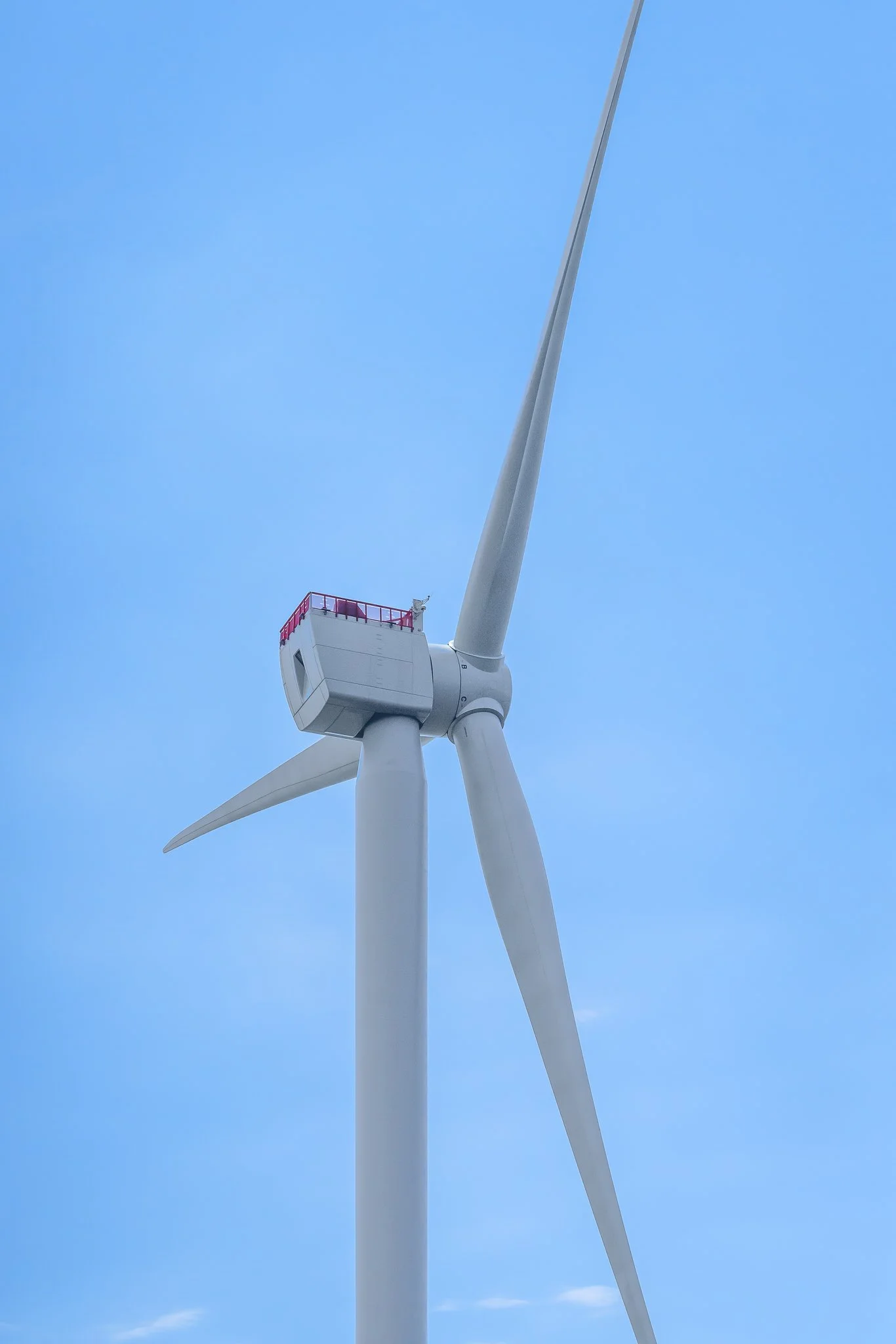 Close-up of a wind turbine's nacelle and hub from the side, with a red railing on top.