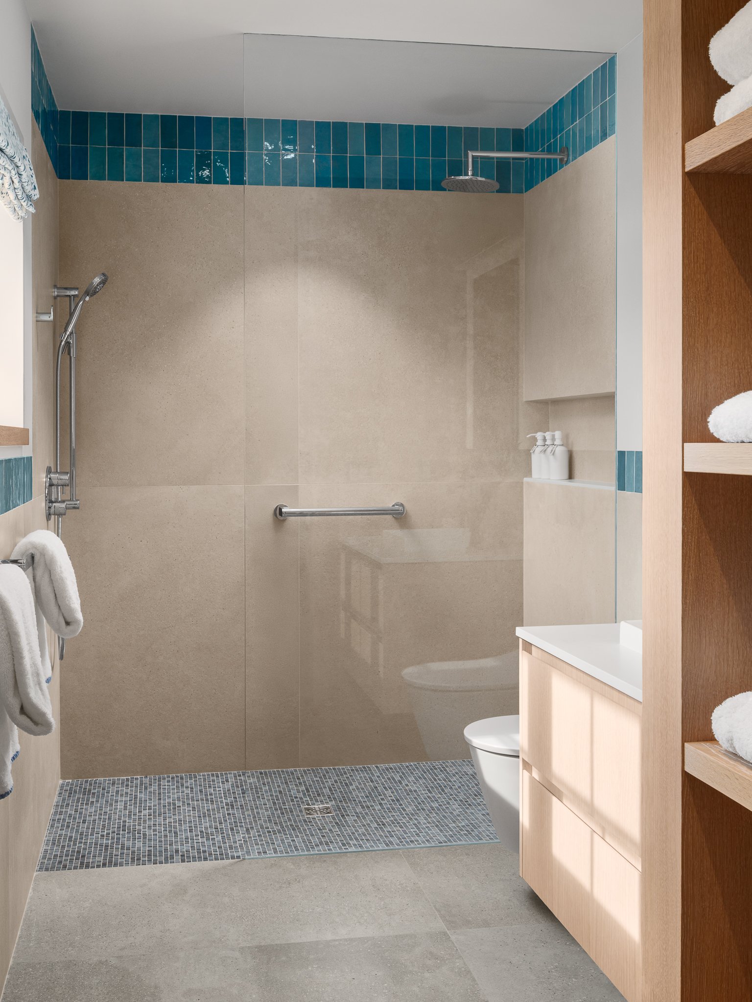 Tan tile bathroom with a glass shower trimmed in blue and a wood vanity.