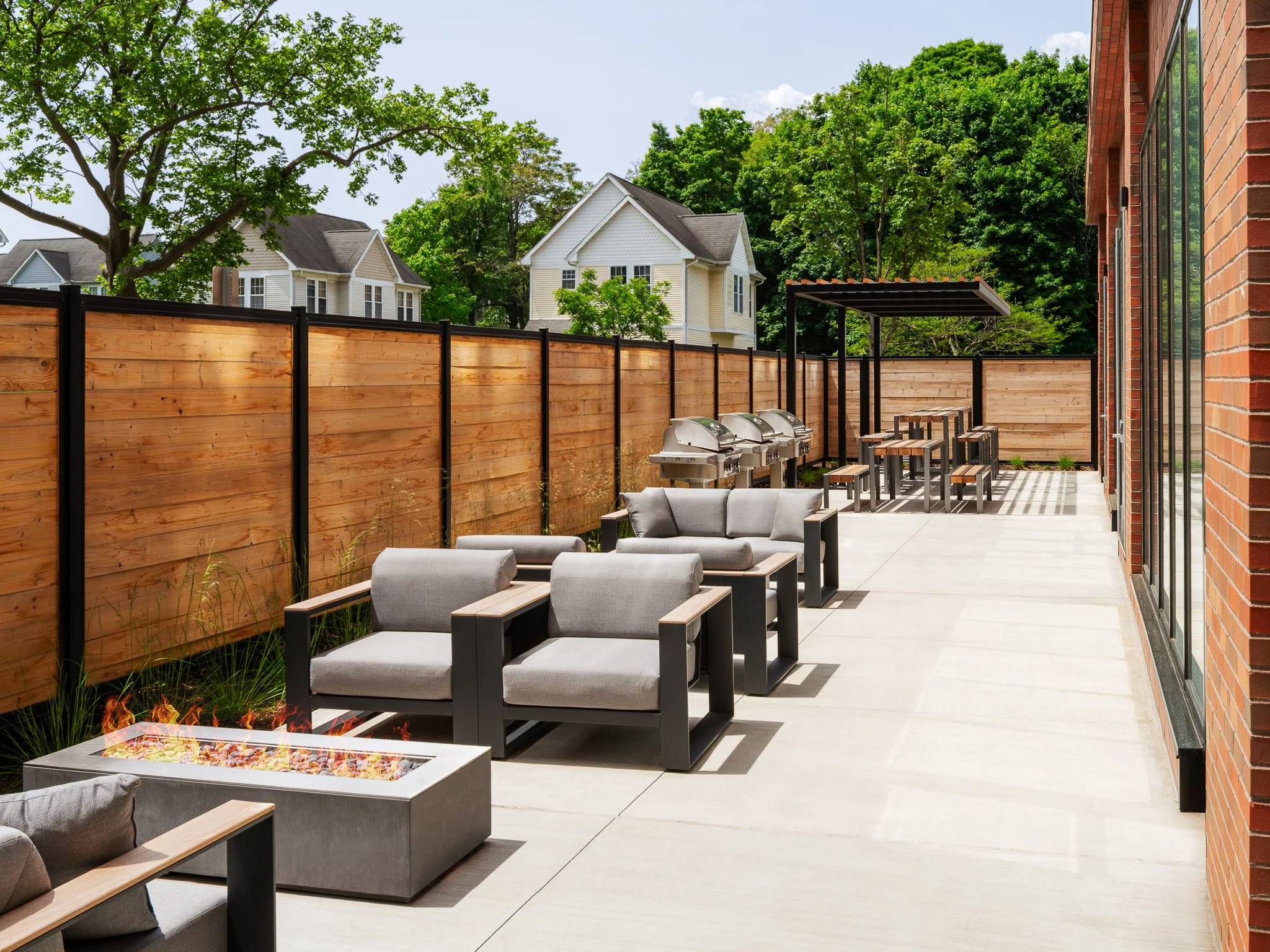Fenced patio with a fire pit, lounge seating, grills and picnic tables.