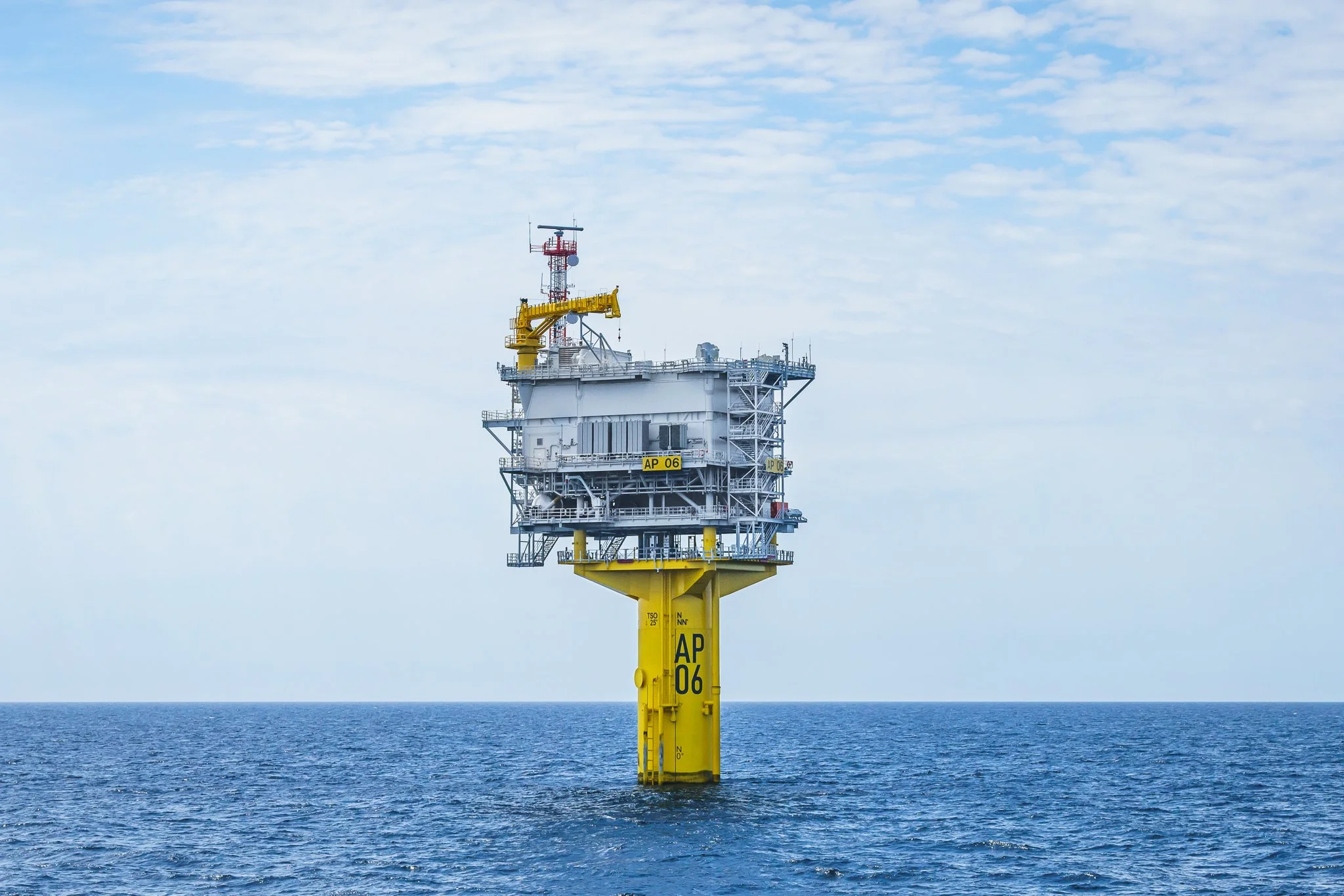 Offshore substation platform with a yellow crane on top, seen level across the water.