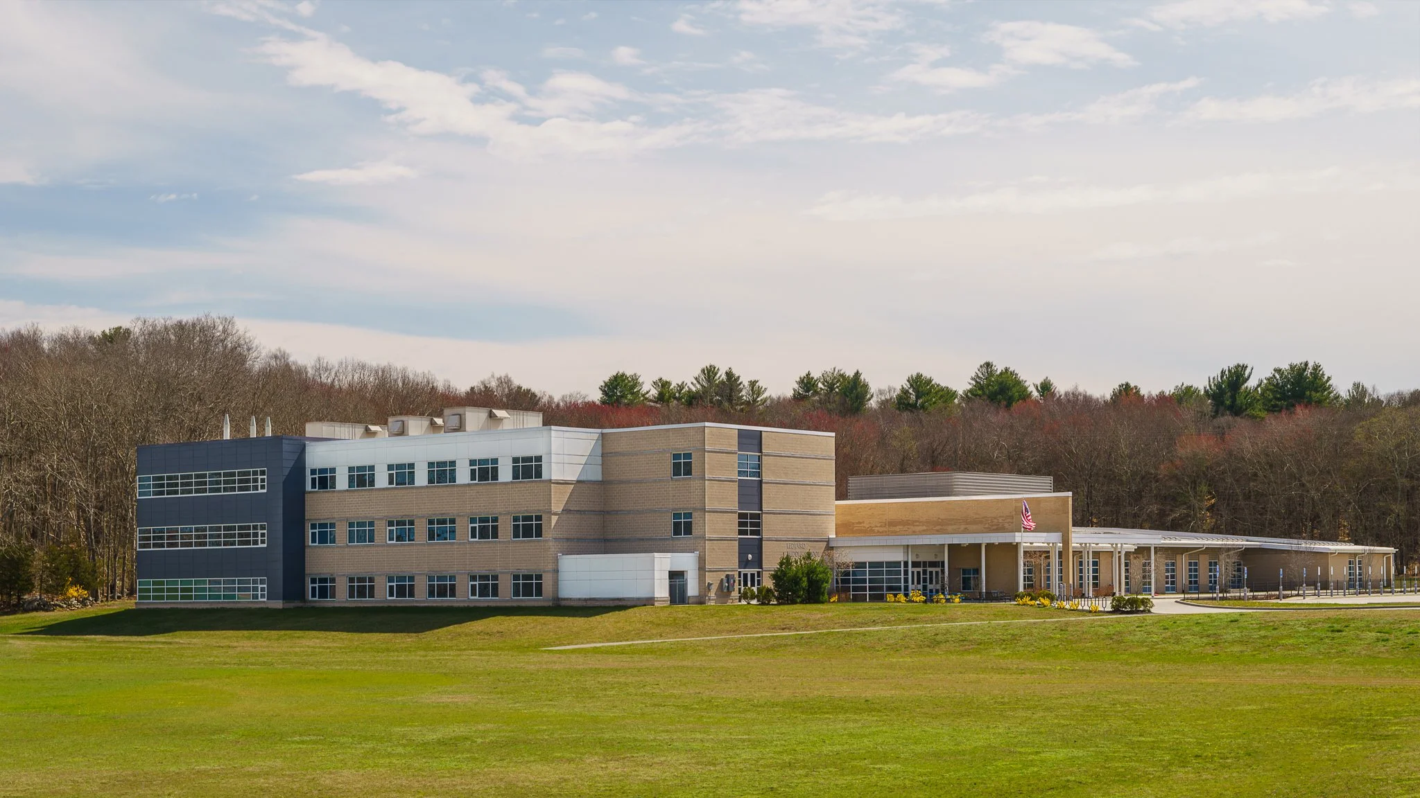 School campus seen across a wide front lawn with wooded hills behind.