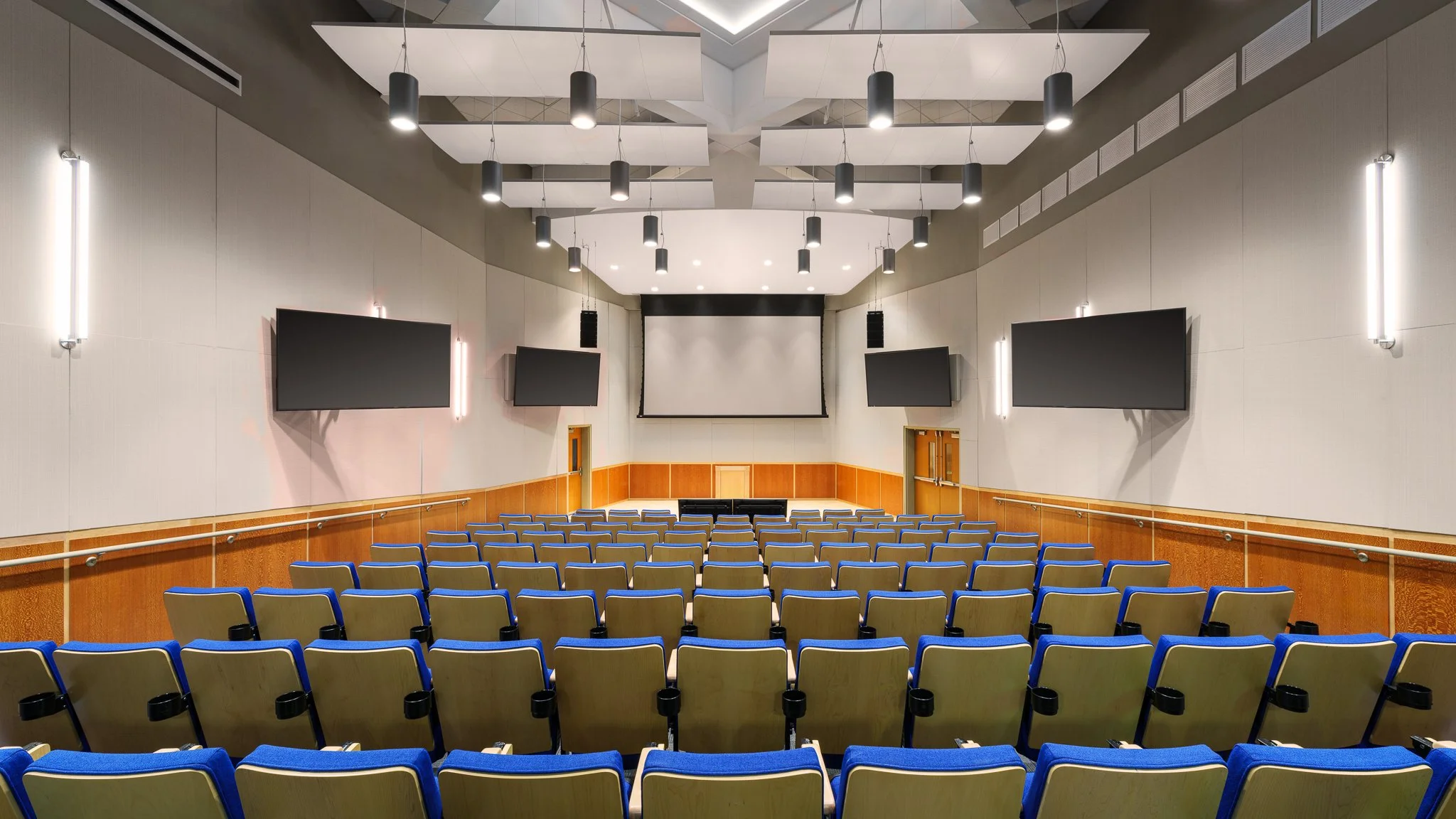Auditorium interior, blue chairs, wall-mounted tv screens, stage, centered projector screen, Groton, CT
