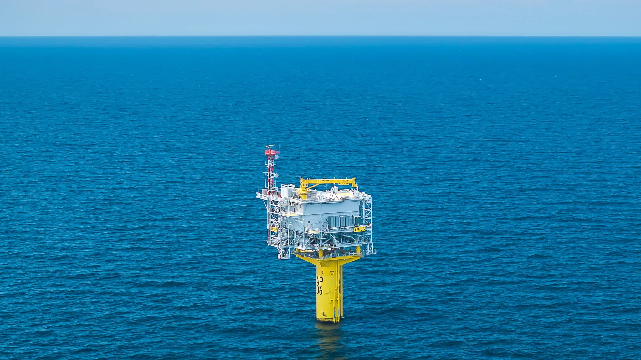 Offshore substation platform on a yellow foundation, seen from above in open water.