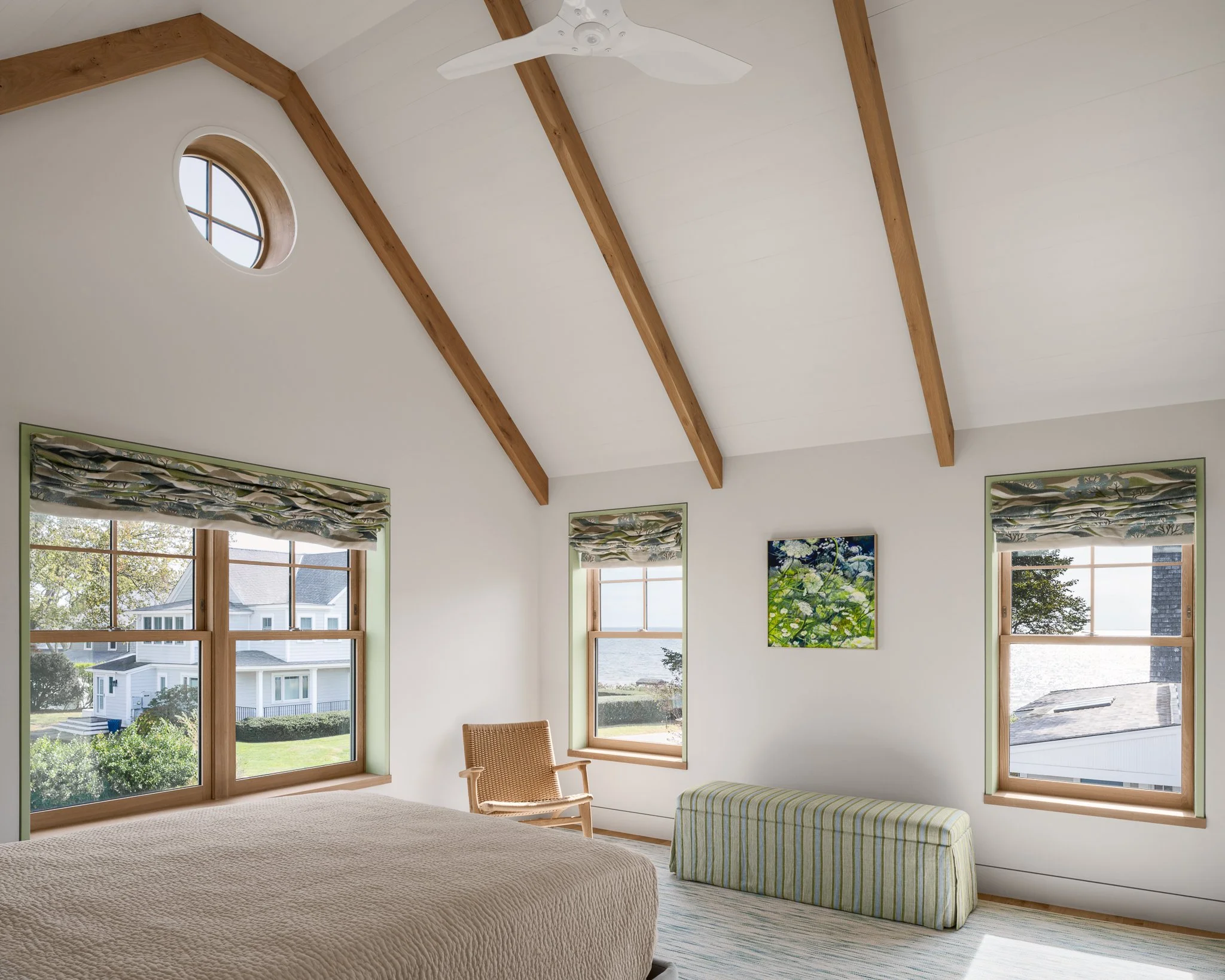 Vaulted guest bedroom with exposed wood beams, a round window and shoreline views.