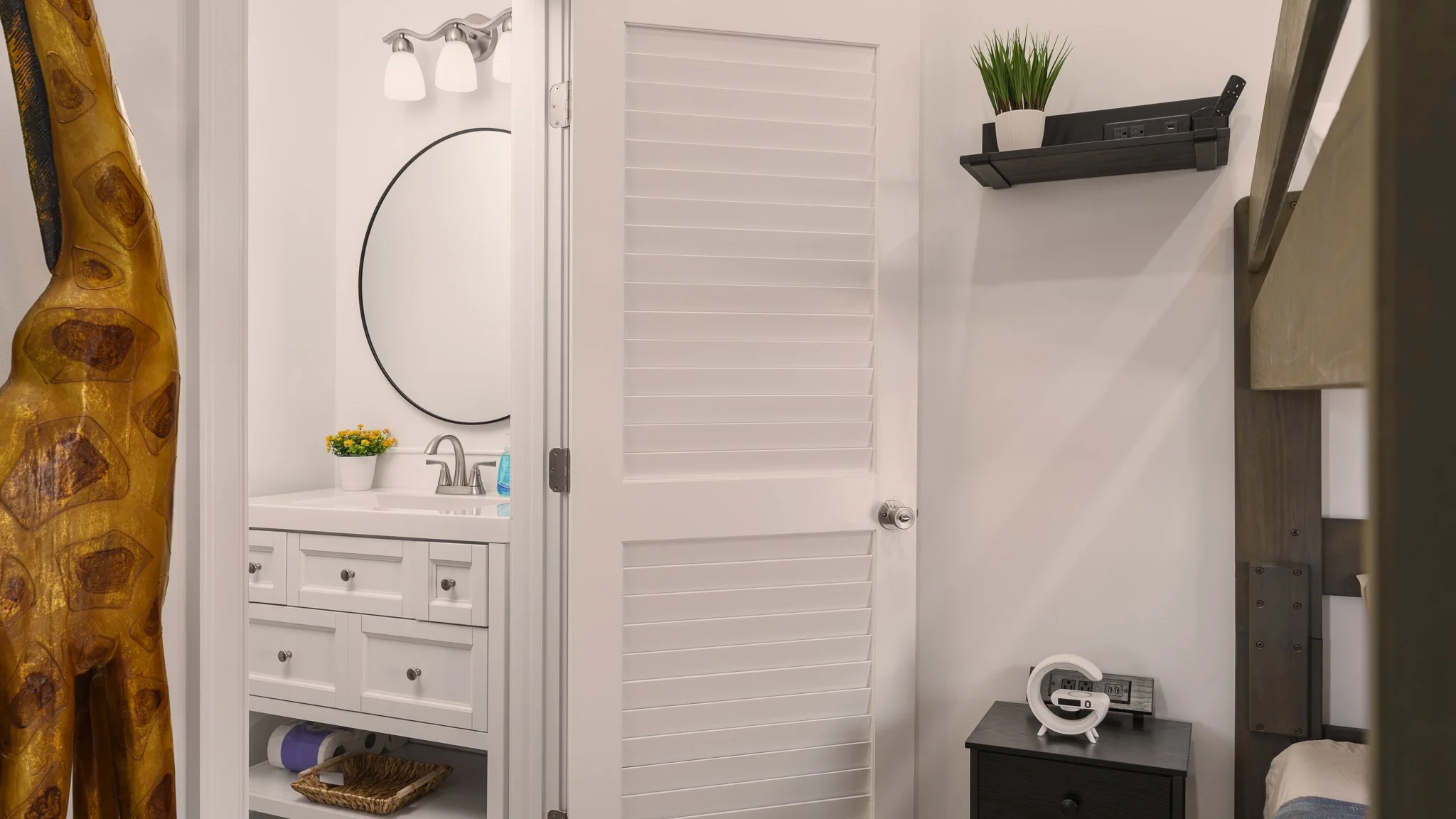 Bedroom corner with a small vanity, round mirror and bathroom door.