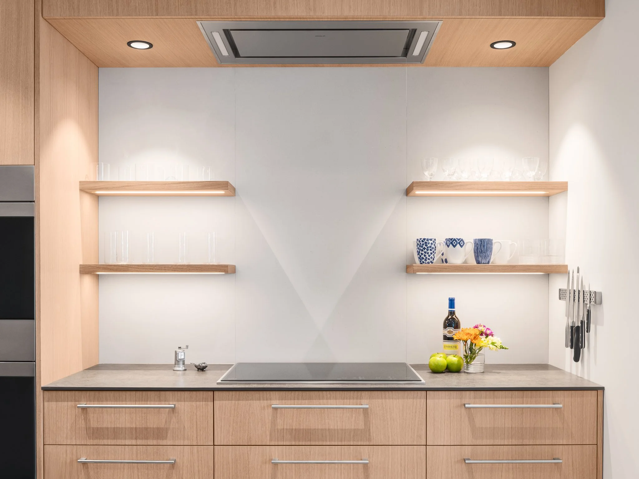 Minimal kitchen wall with a cooktop, wood base cabinets and two floating shelves.