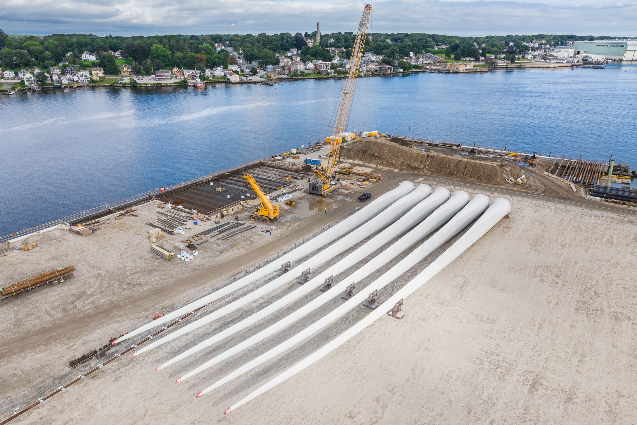 Aerial drone view of a crane and wind turbine blades along the waterfront.