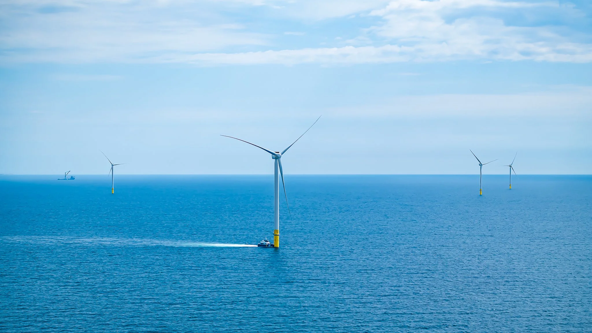 Wide view of a crew vessel at a turbine base with four more turbines along the horizon.