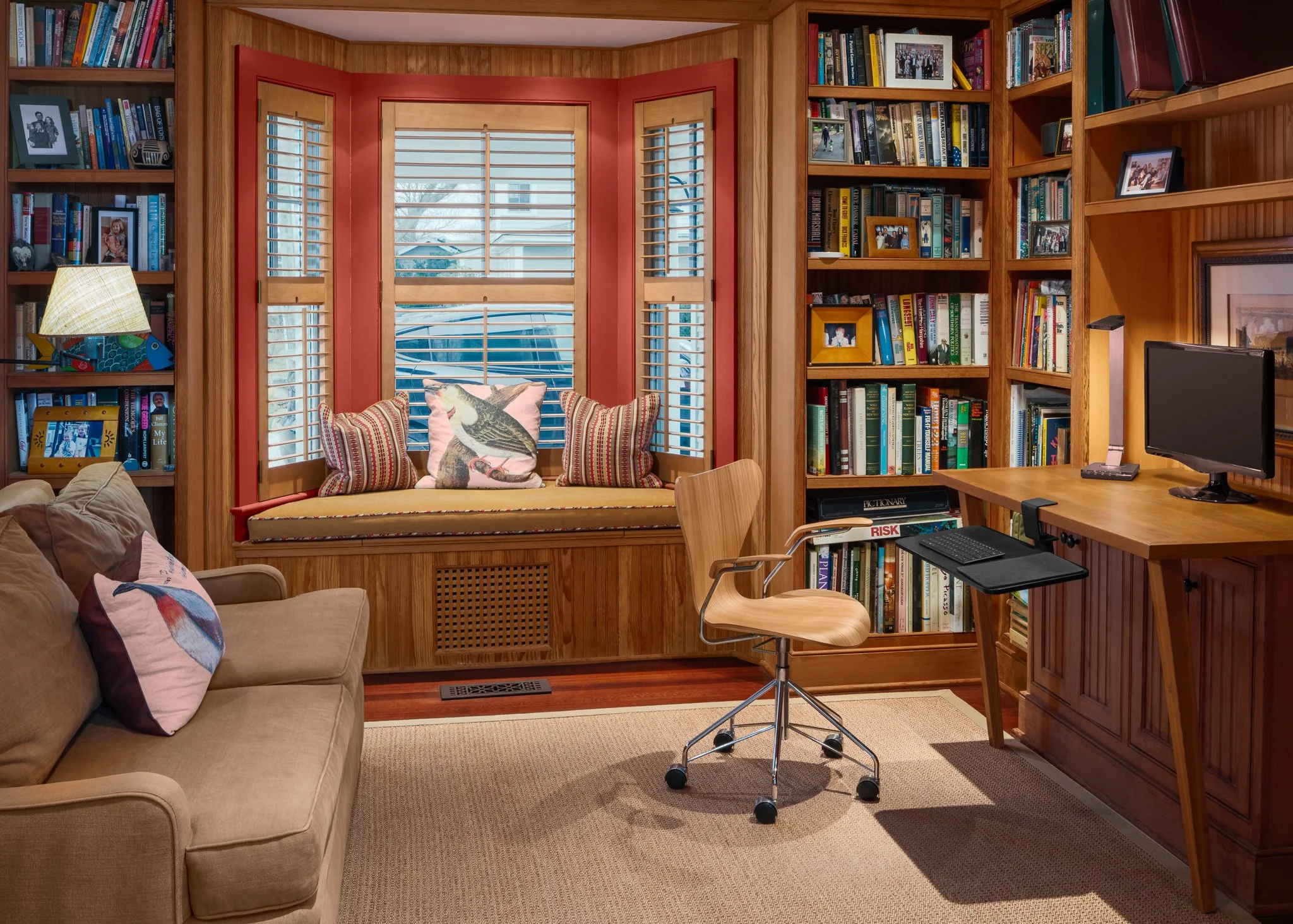 Wood-paneled study with floor to ceiling bookshelves, a desk and a cushioned bay window.