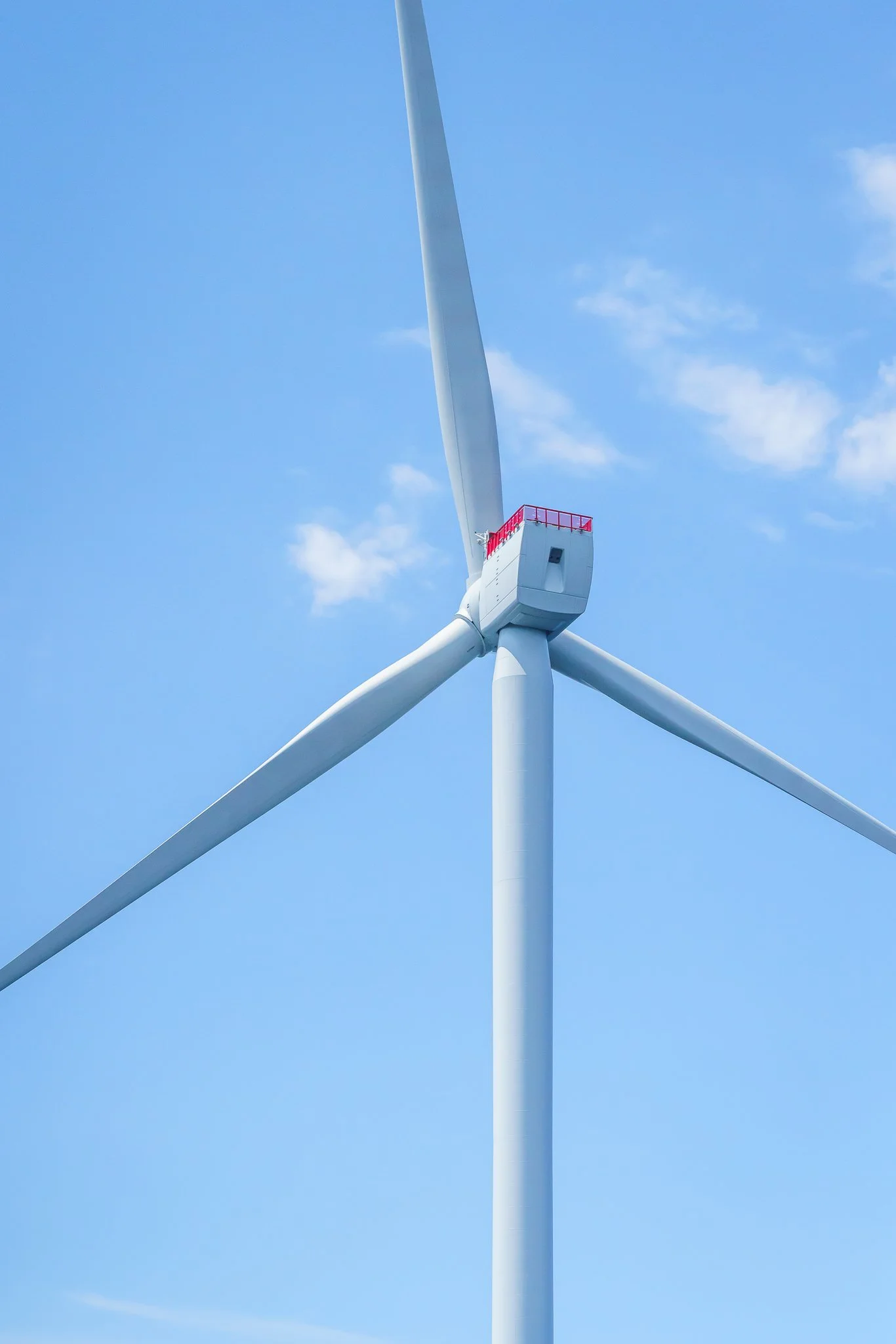 Front view of a wind turbine hub and blades against blue sky with small clouds.