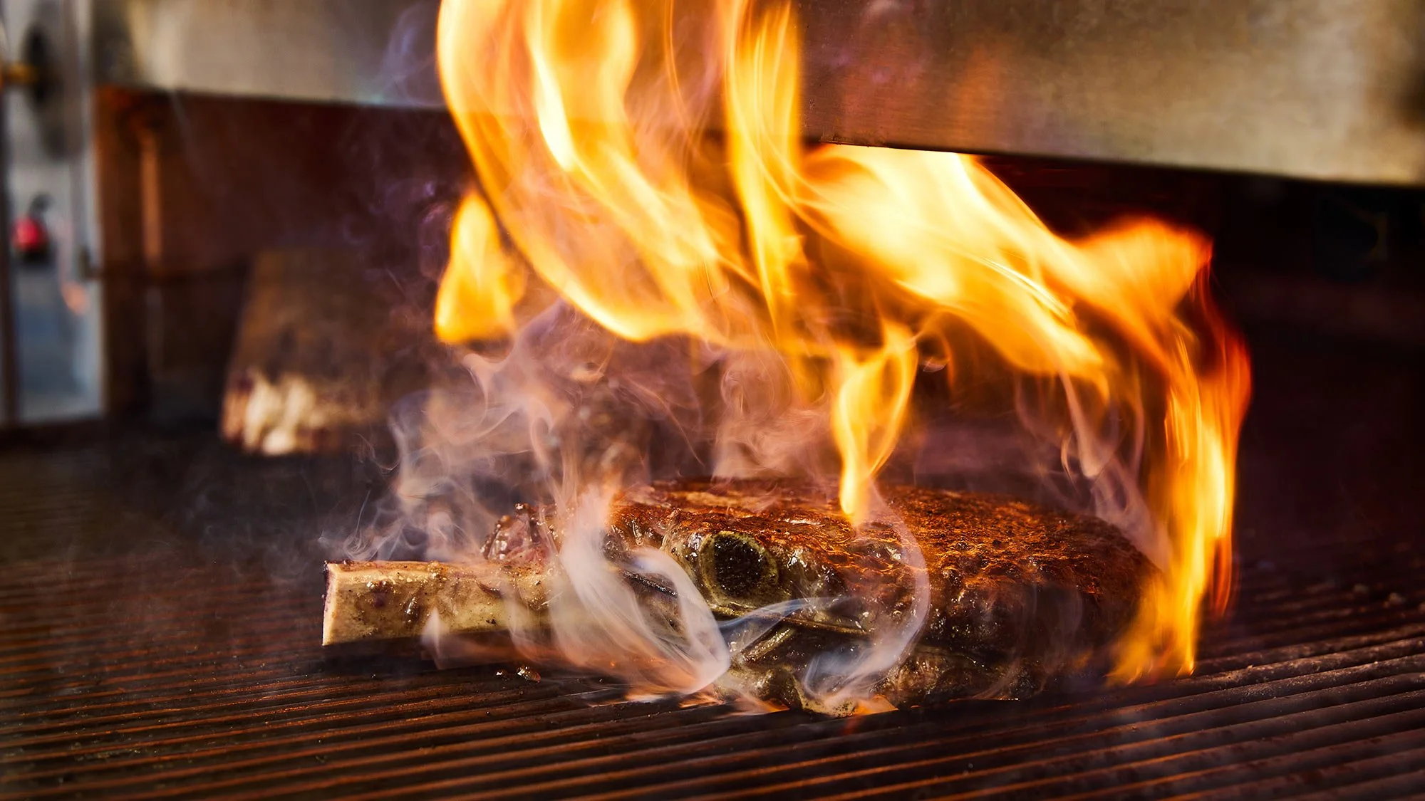 A steak on a grill with flames and smoke.