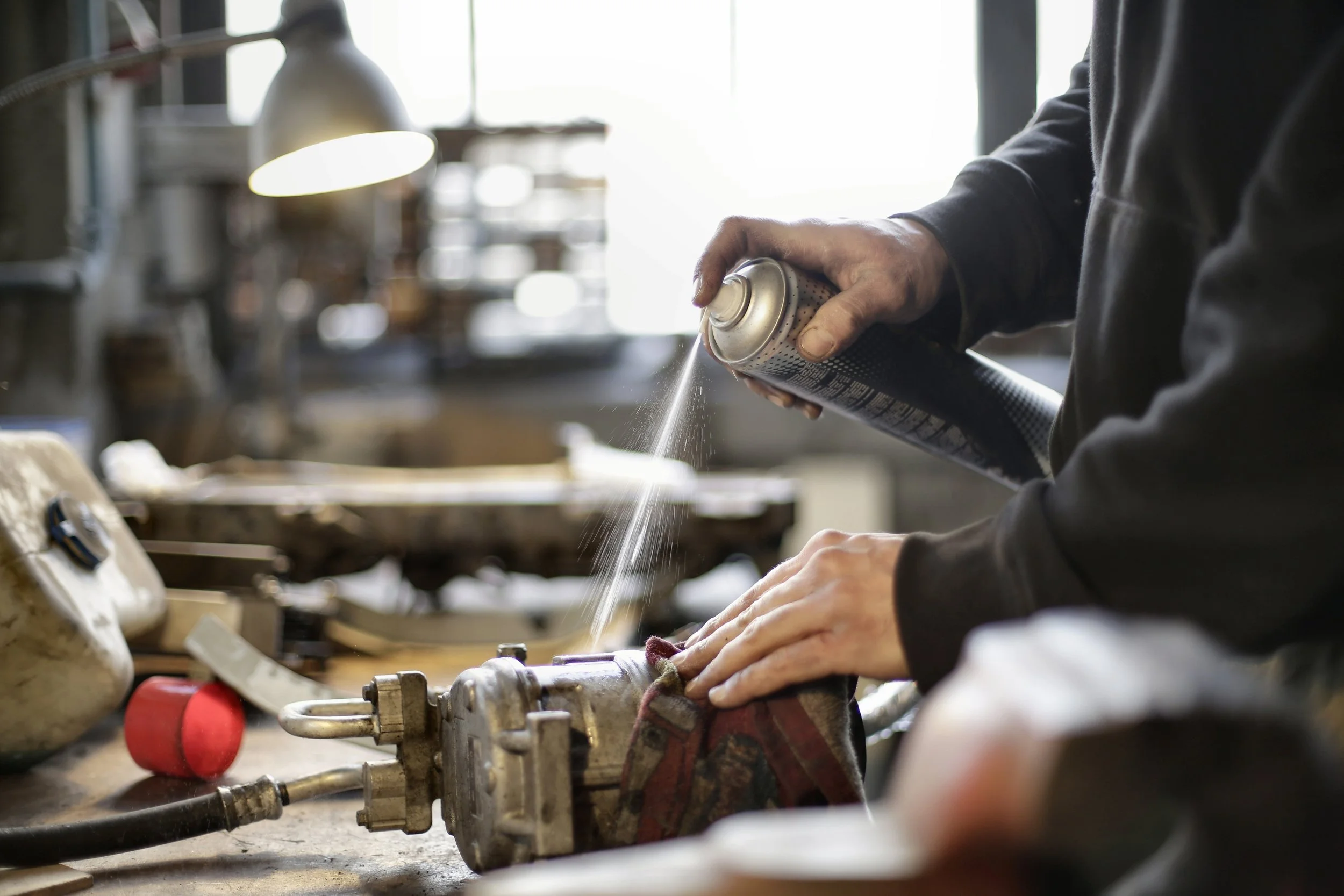 Canadian Work Permit Mechanic holding lubricant bottle over machined part