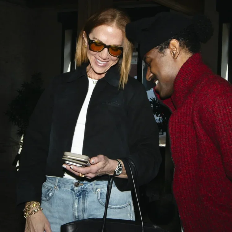 Sarah Schmidt wearing a red jacket and sunglasses engages in conversation with a man.