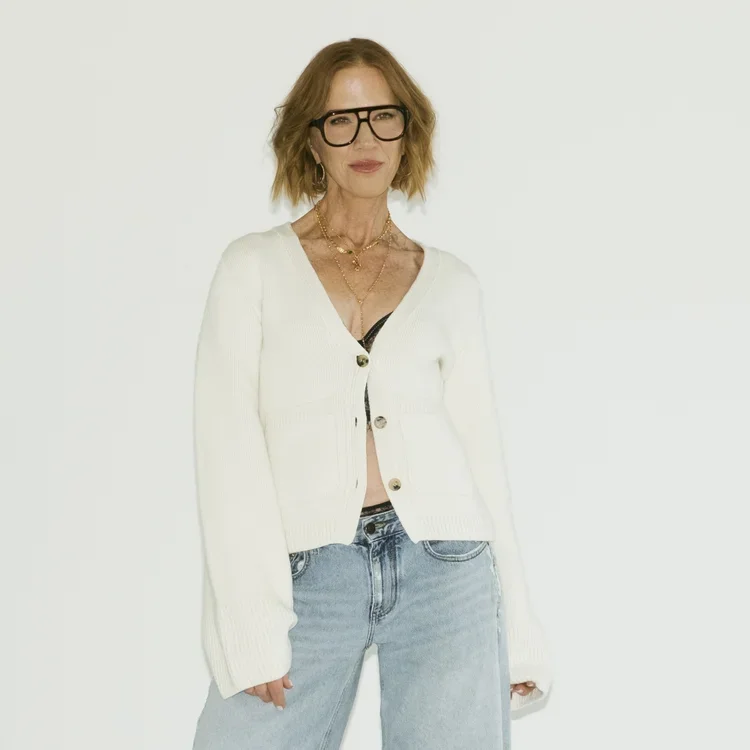 Sarah Schmidt wearing a white sweater and jeans stands confidently, smiling at the camera.