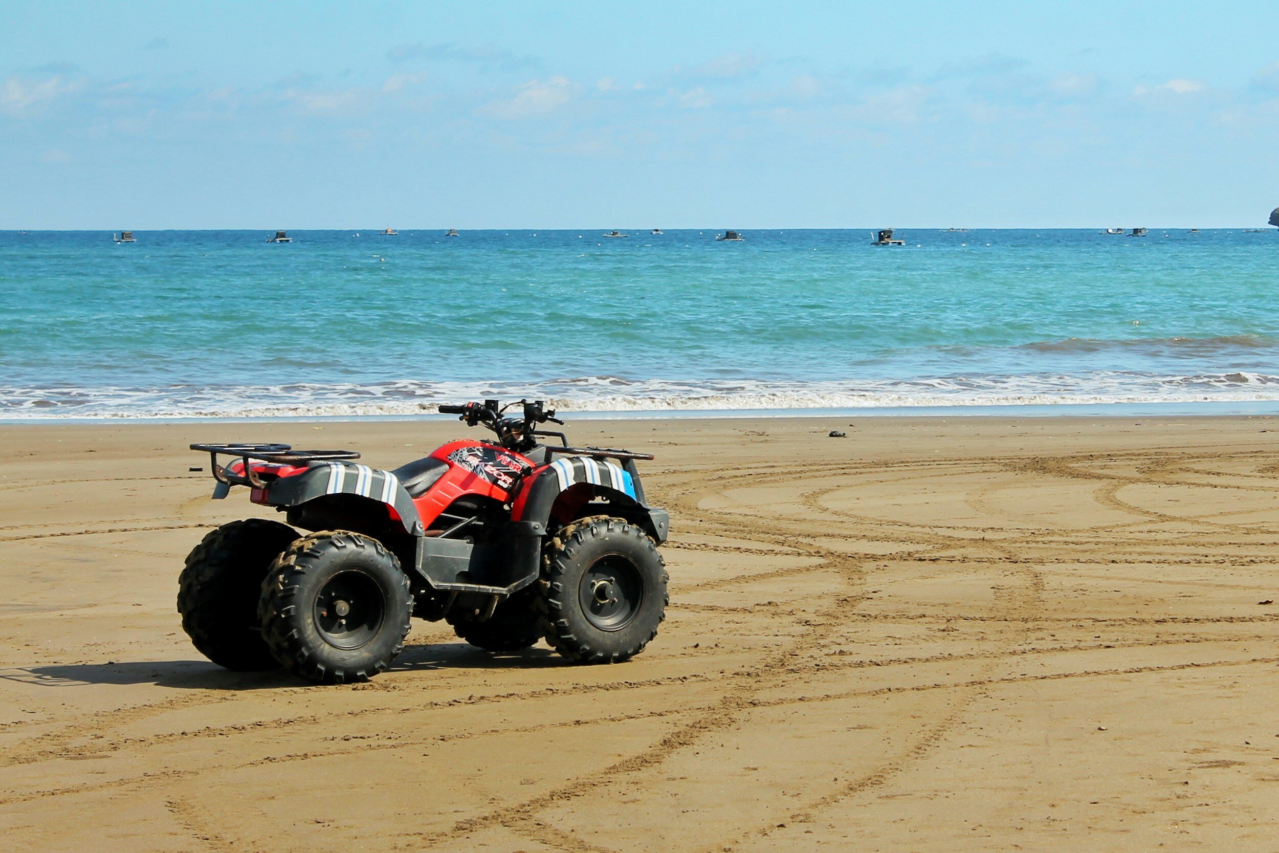 All-terrain vehicle on a sandy beach facing the ocean with a clear sky.