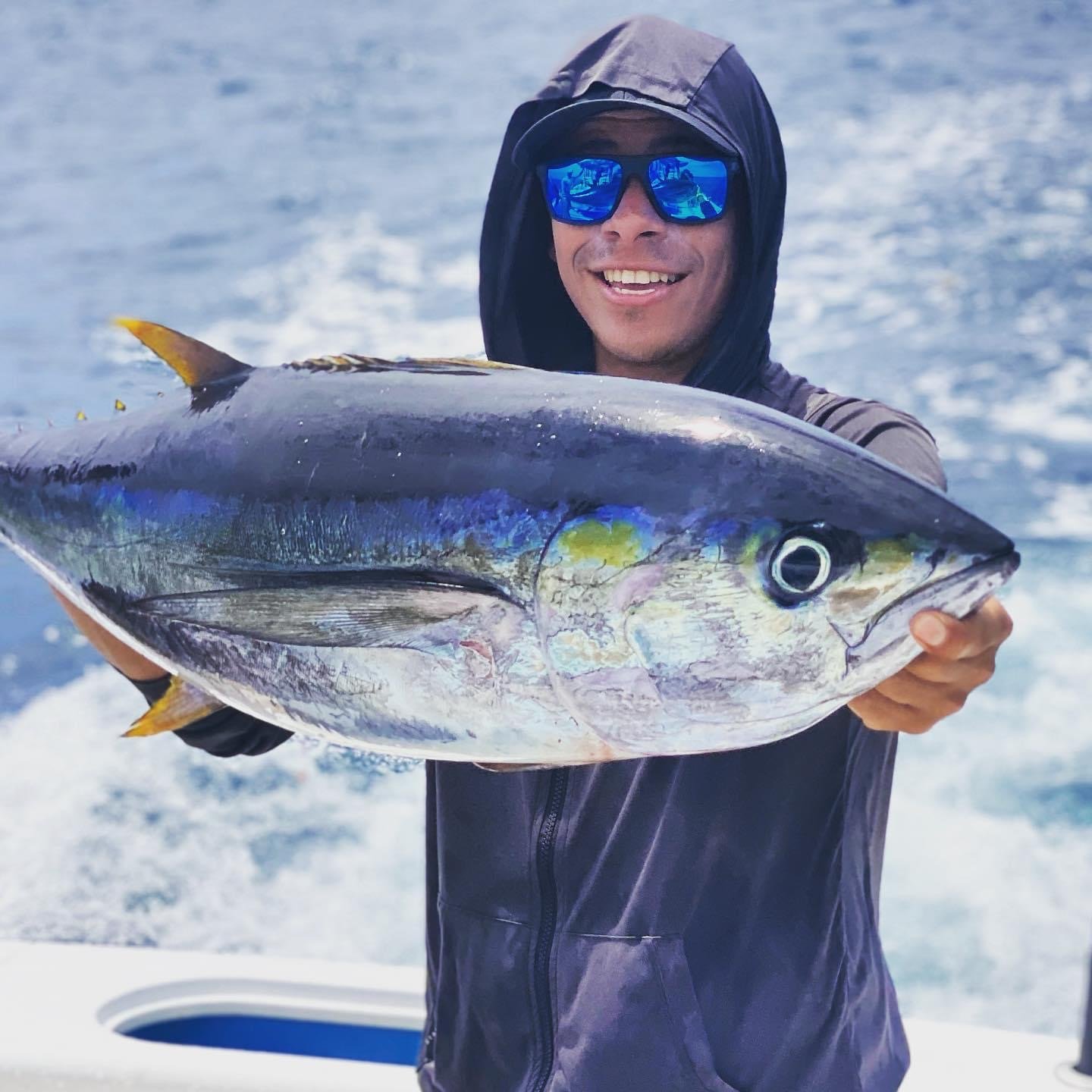Person holding a large fish, possibly a tuna, on a boat.