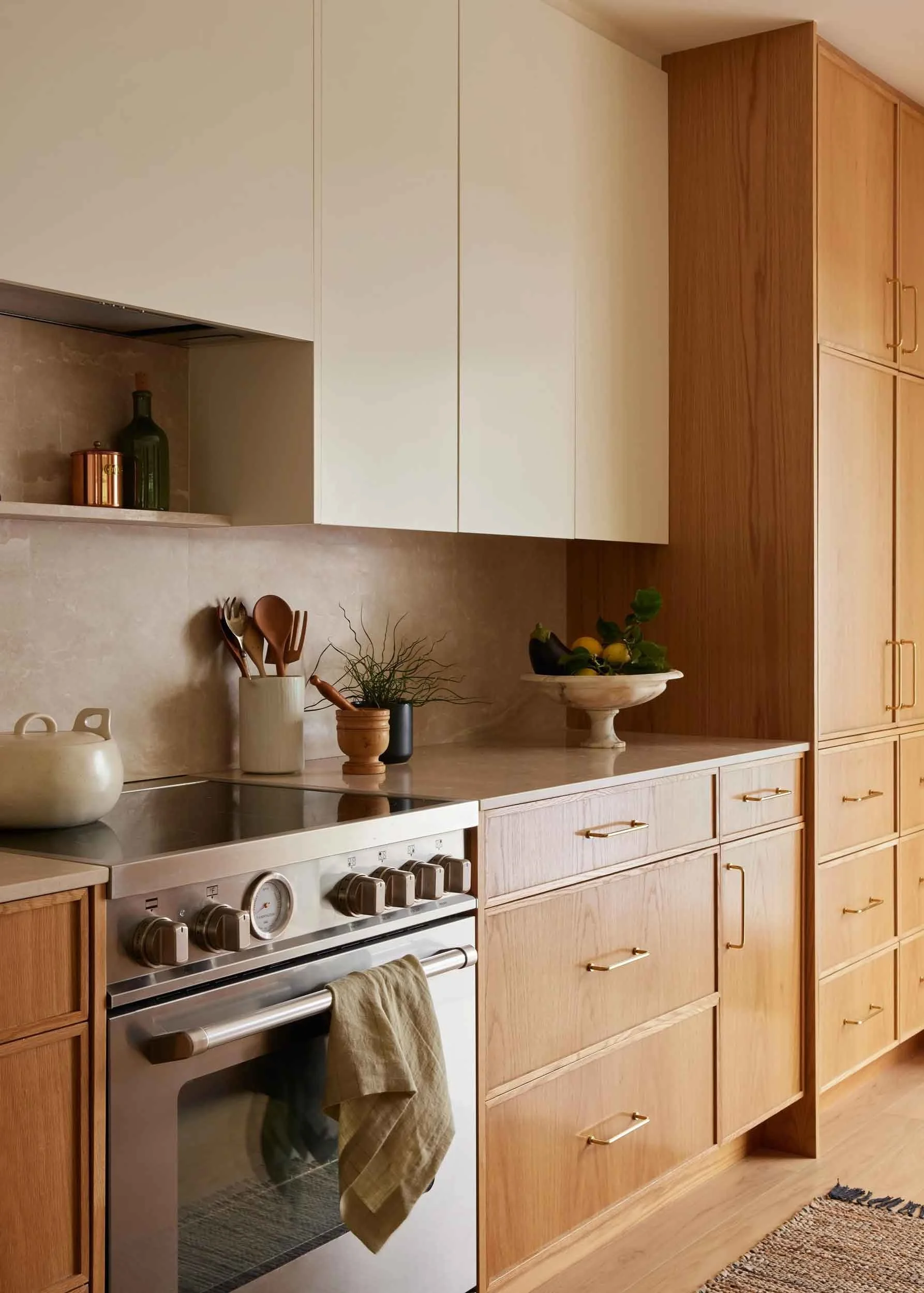 Modern kitchen with wooden cabinets, stainless steel oven, countertop accessories, and decorative fruit bowl.