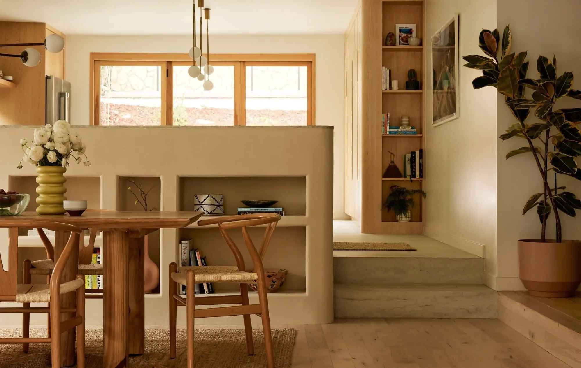 Modern dining room with wooden table and chairs, built-in shelving, potted plant, and pendant lights