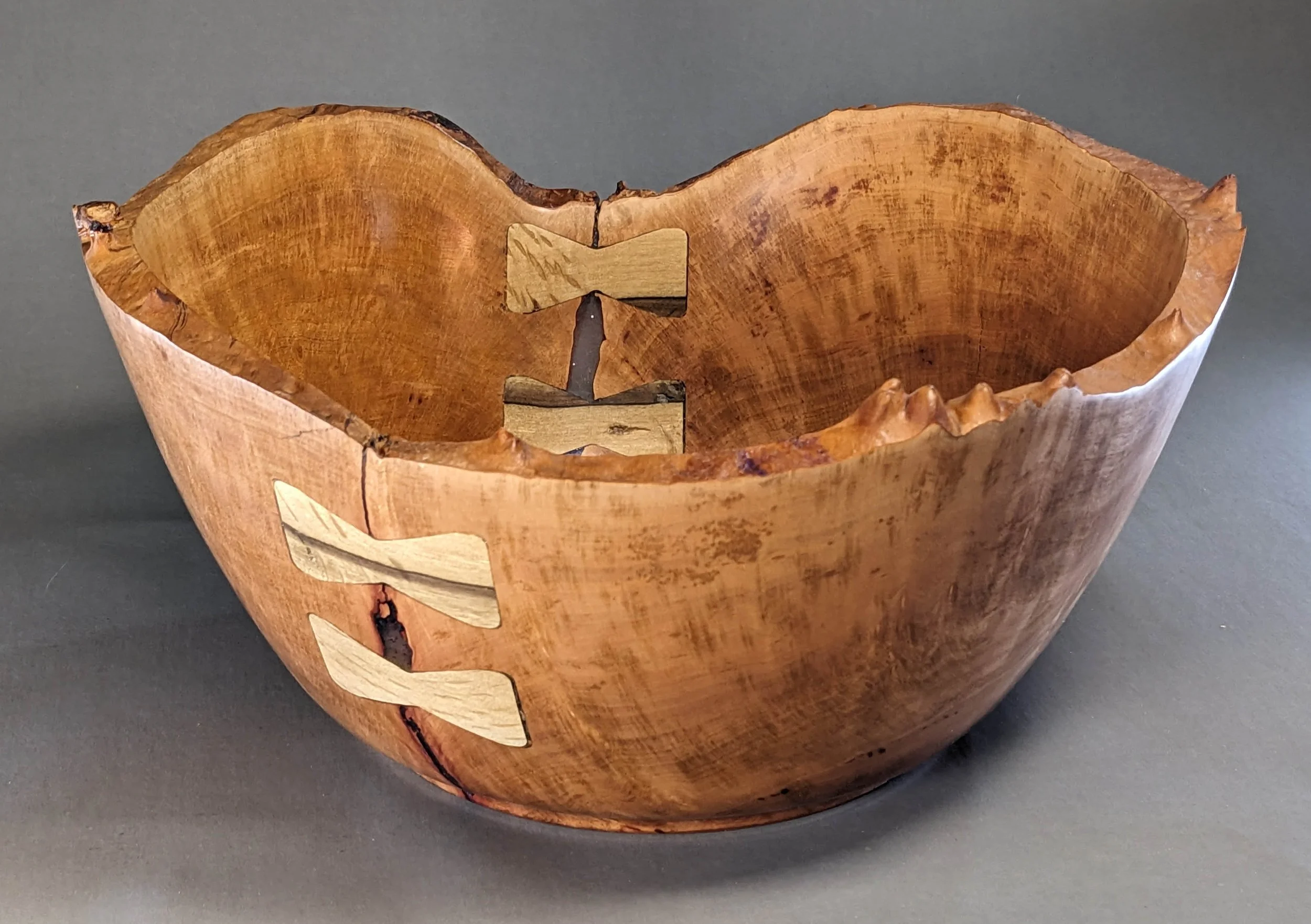 This hand-turned bowl showcases the rich, warm tones of seasoned Madrone wood. The natural-rim preserves the original character of the tree, while the intricate grain is accentuated by decorative butterfly inlets and subtle epoxy fillings. Finished w