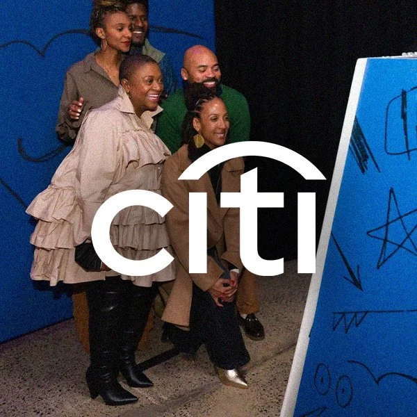 Group of five smiling people taking a selfie in front of a blue wall and a large drawing board with scribbles.